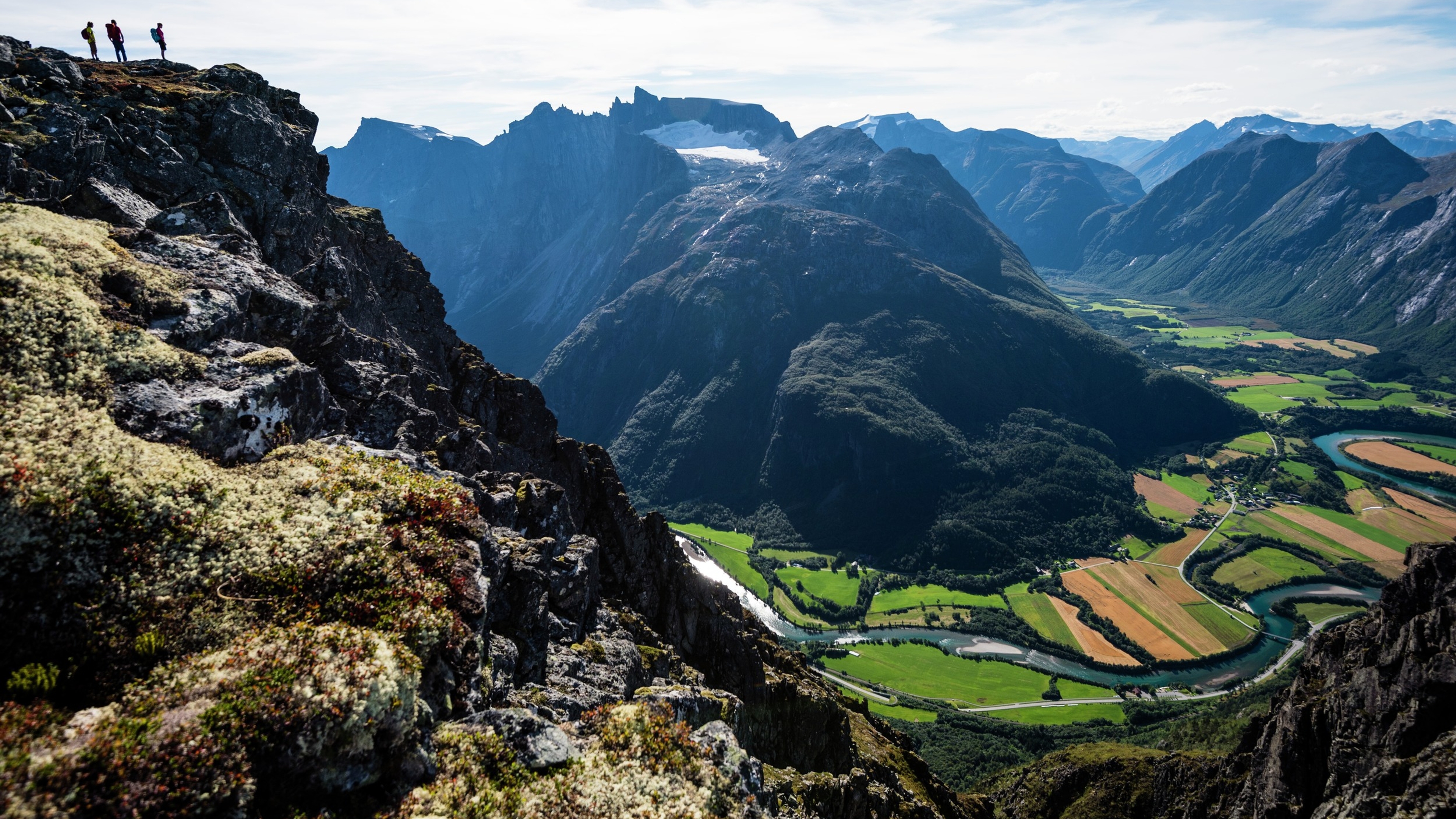 Three hikers seen looking out at the view from the Romsdalseggen ridge in Åndalsnes in Northwest, Fjord Norway
