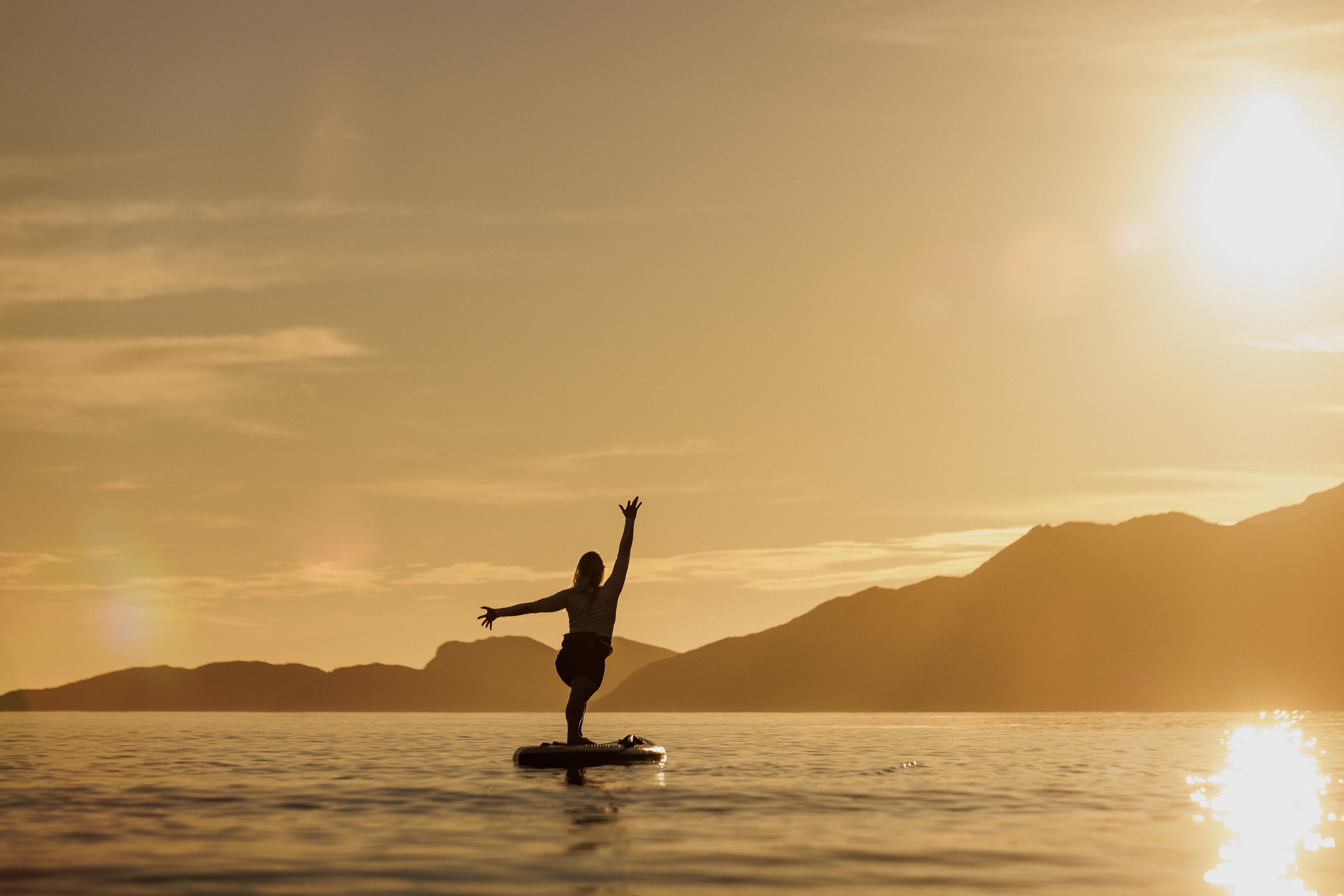 A woman doing yoga on a paddle board in the midnight sun, Northern Norway.