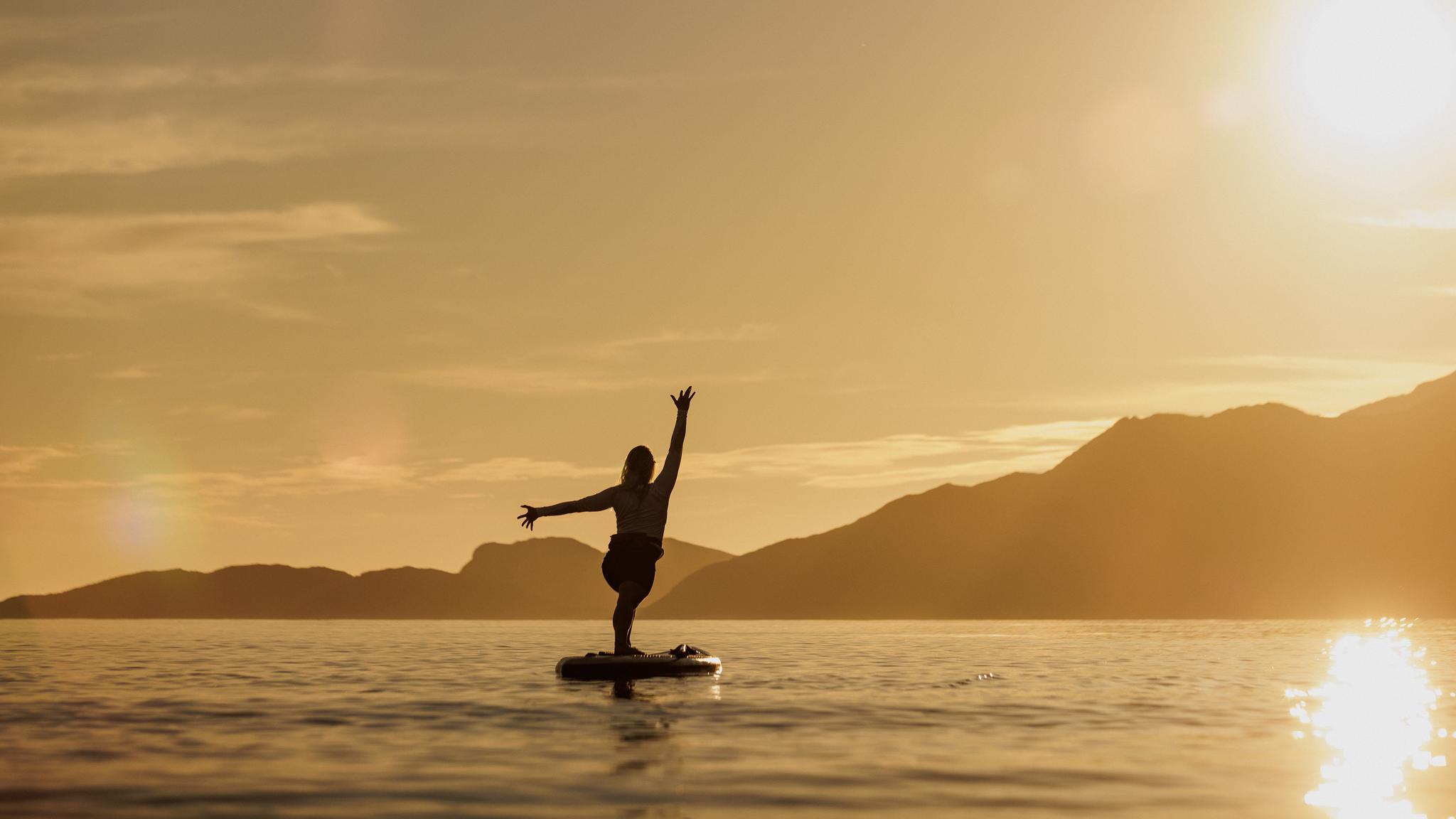 A woman doing yoga on a paddle board in the midnight sun, Northern Norway.