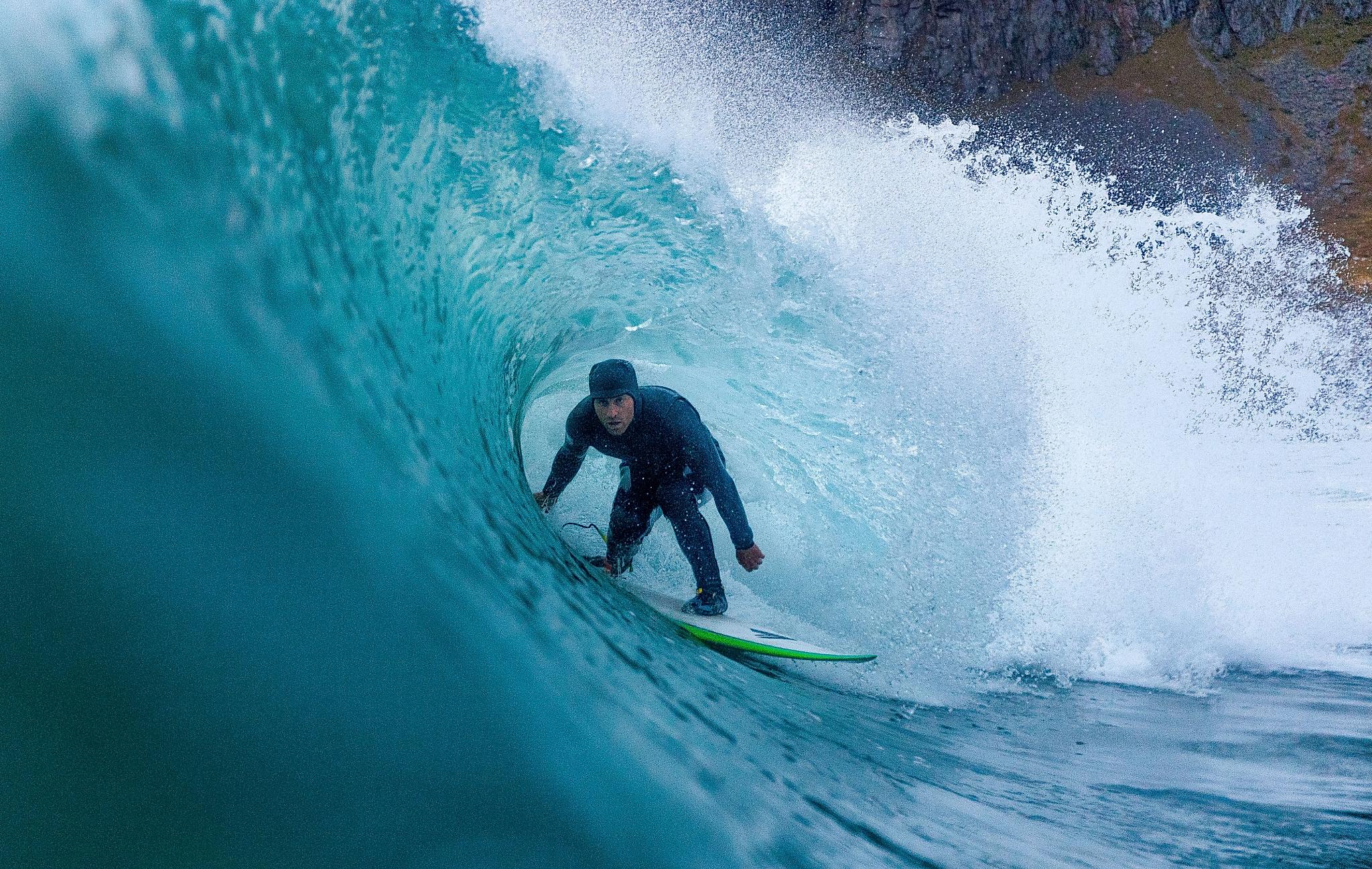 A surfer riding under a breaking wave on Lofoten islands in Northern Norway
