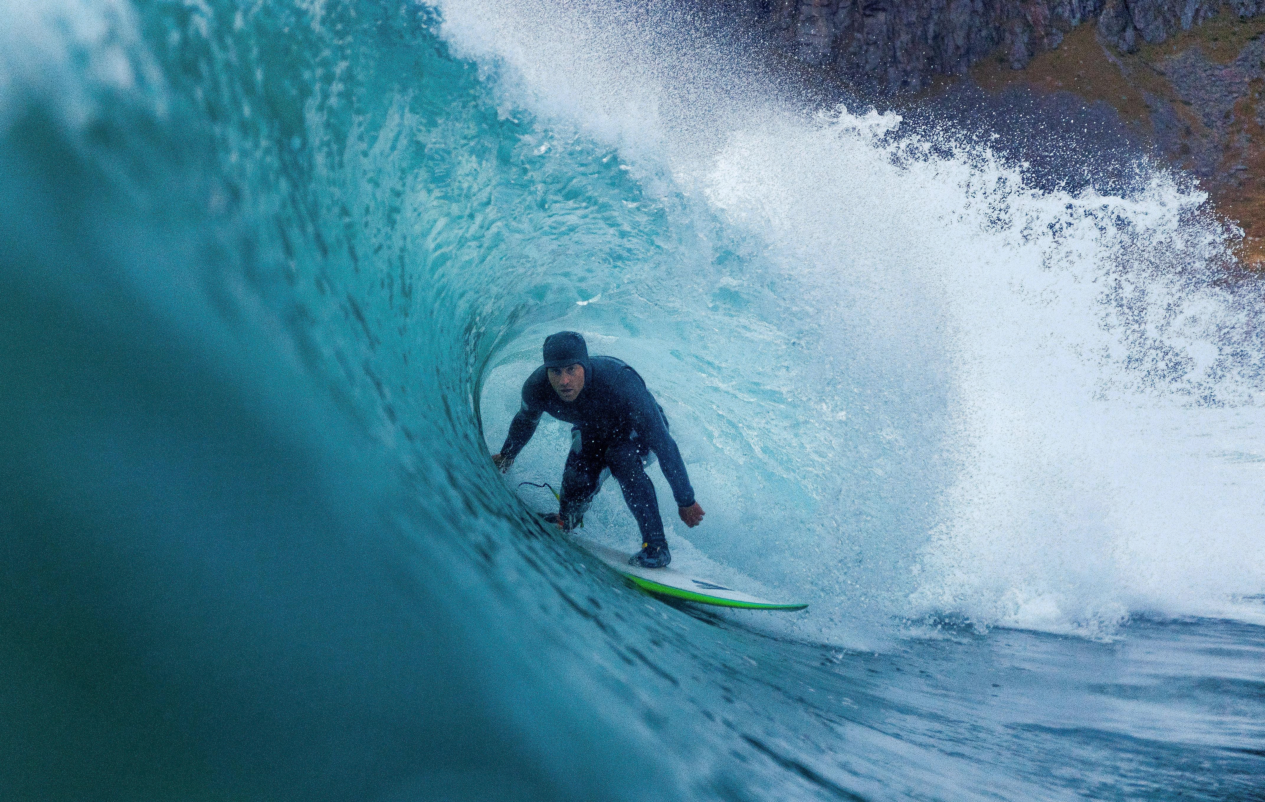 A surfer riding under a breaking wave on Lofoten islands in Northern Norway