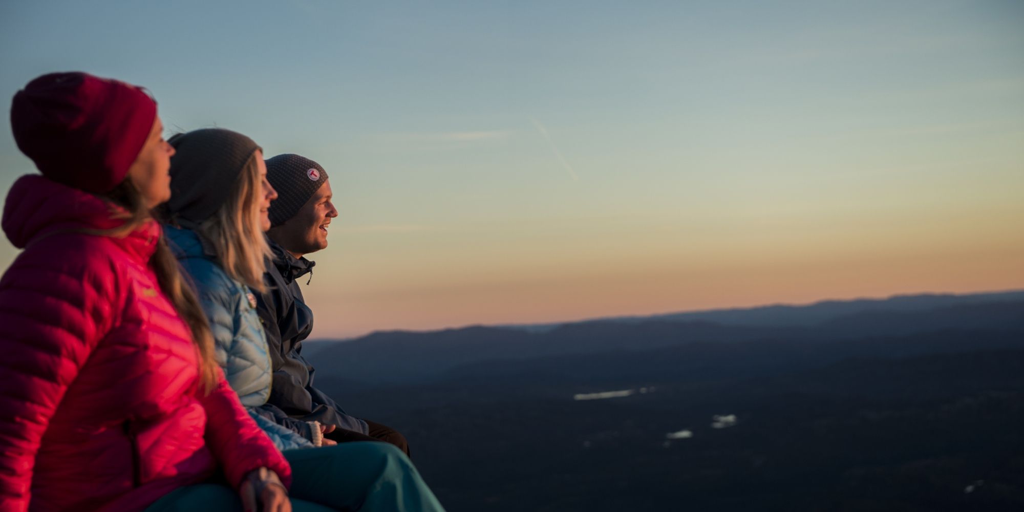 Drie mensen bewonderen het uitzicht tijdens de zonsopgang vanaf de berg Gaustatoppen in Telemark, Oost-Noorwegen
