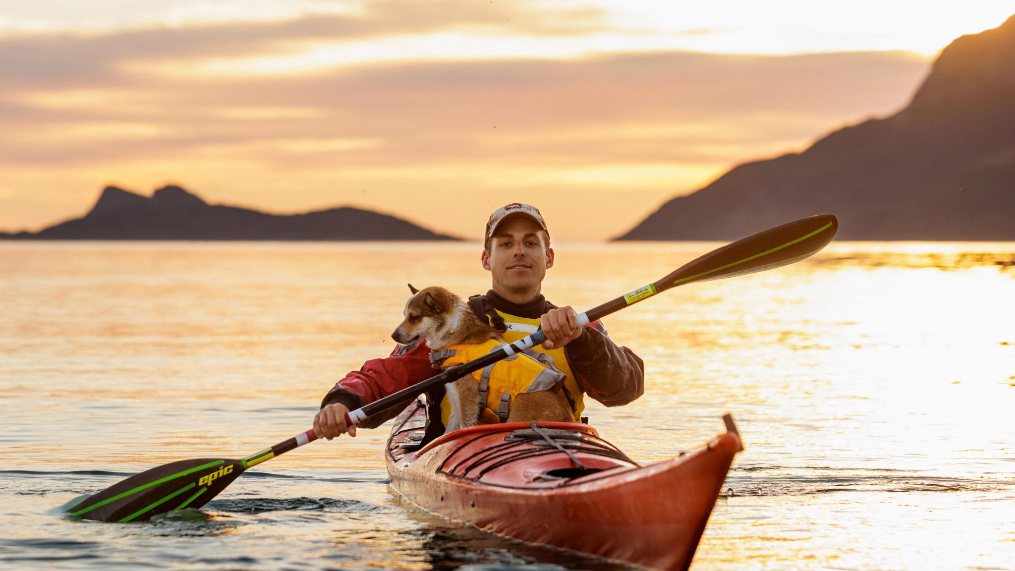 A man and a dog is kayaking in the midnight sun in Northern Norway.