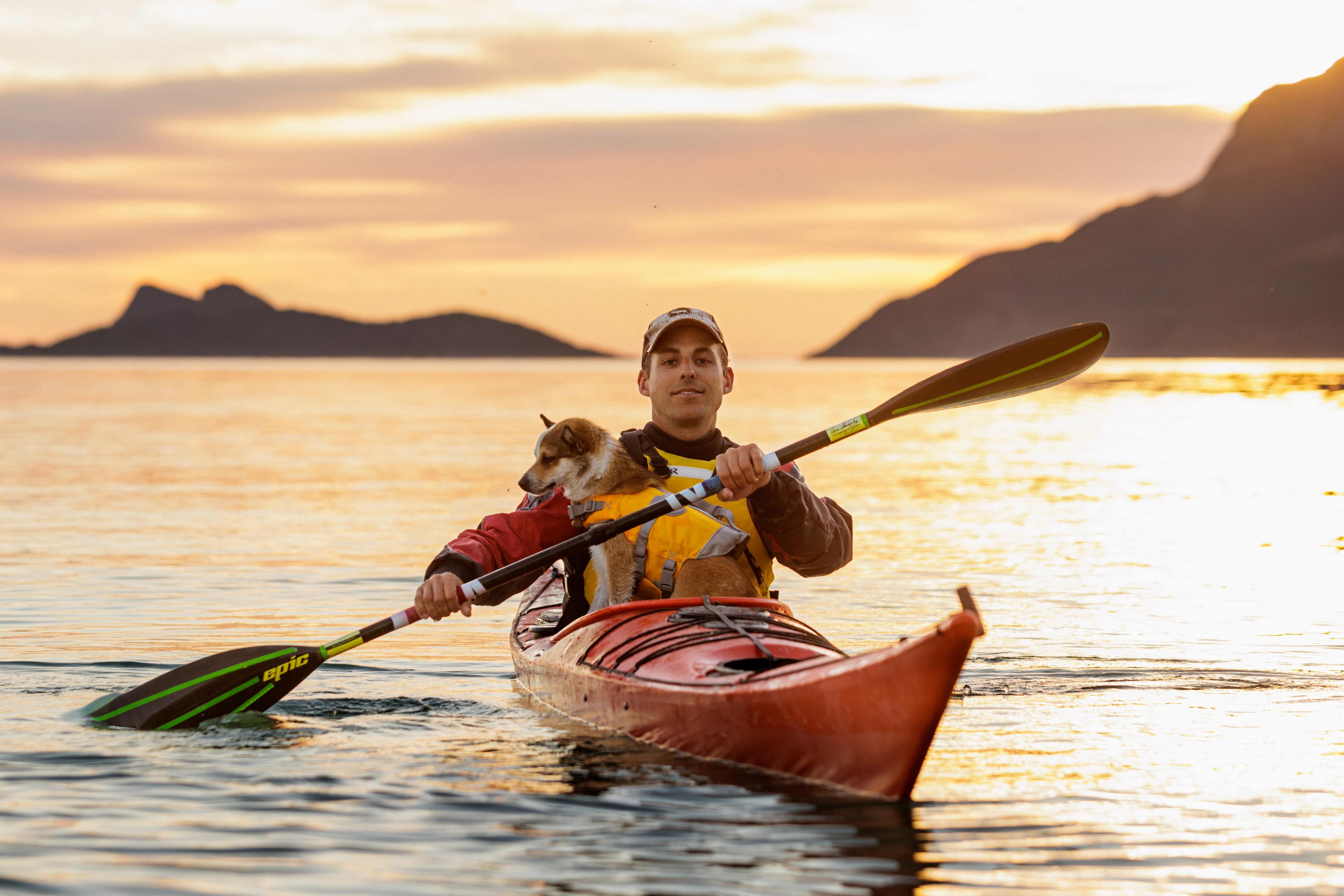 A man and a dog is kayaking in the midnight sun in Northern Norway.