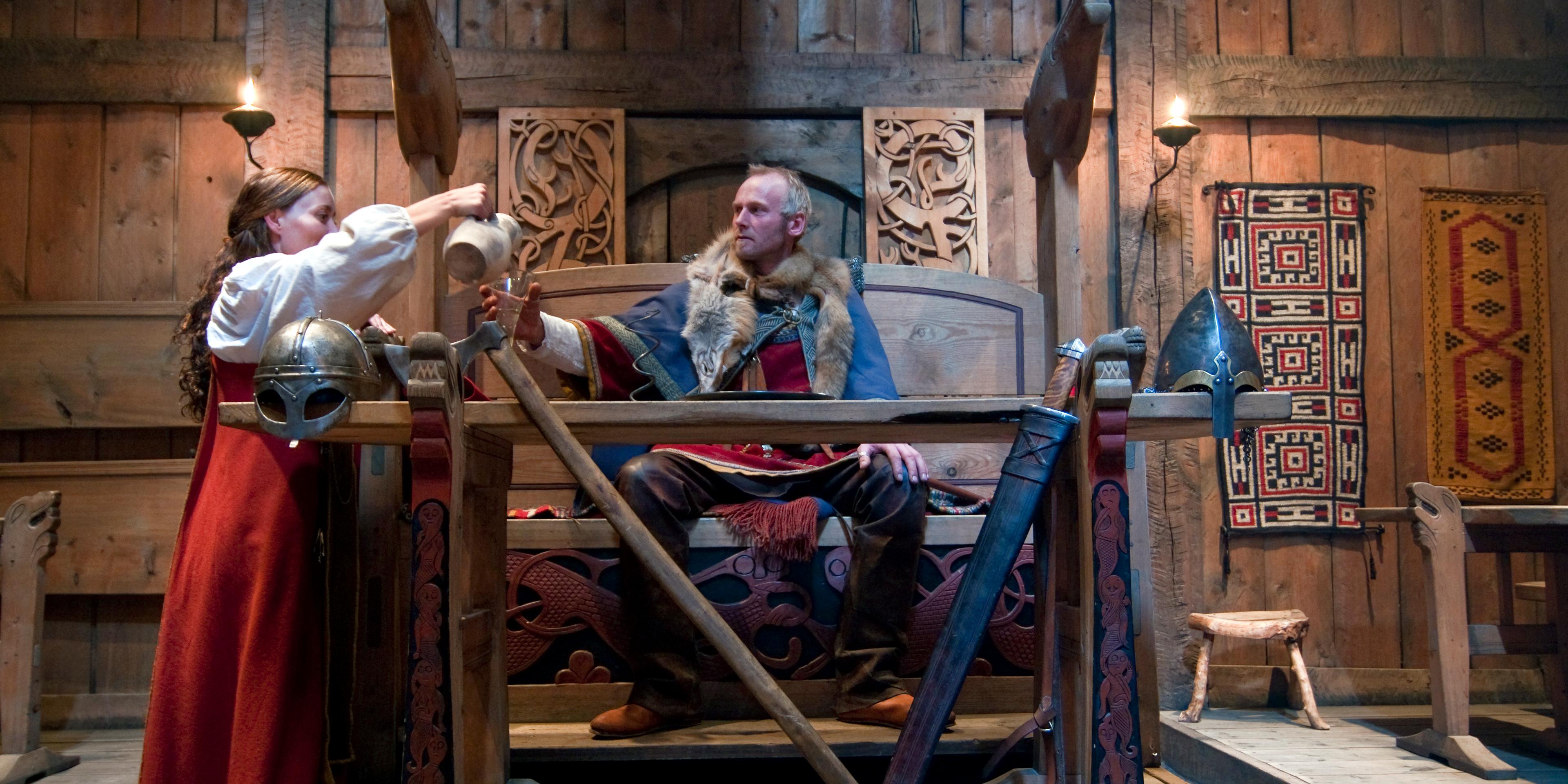 Viking throne with man and woman dressed as vikings in the Lofotr Viking Museum in Lofoten, Northern Norway