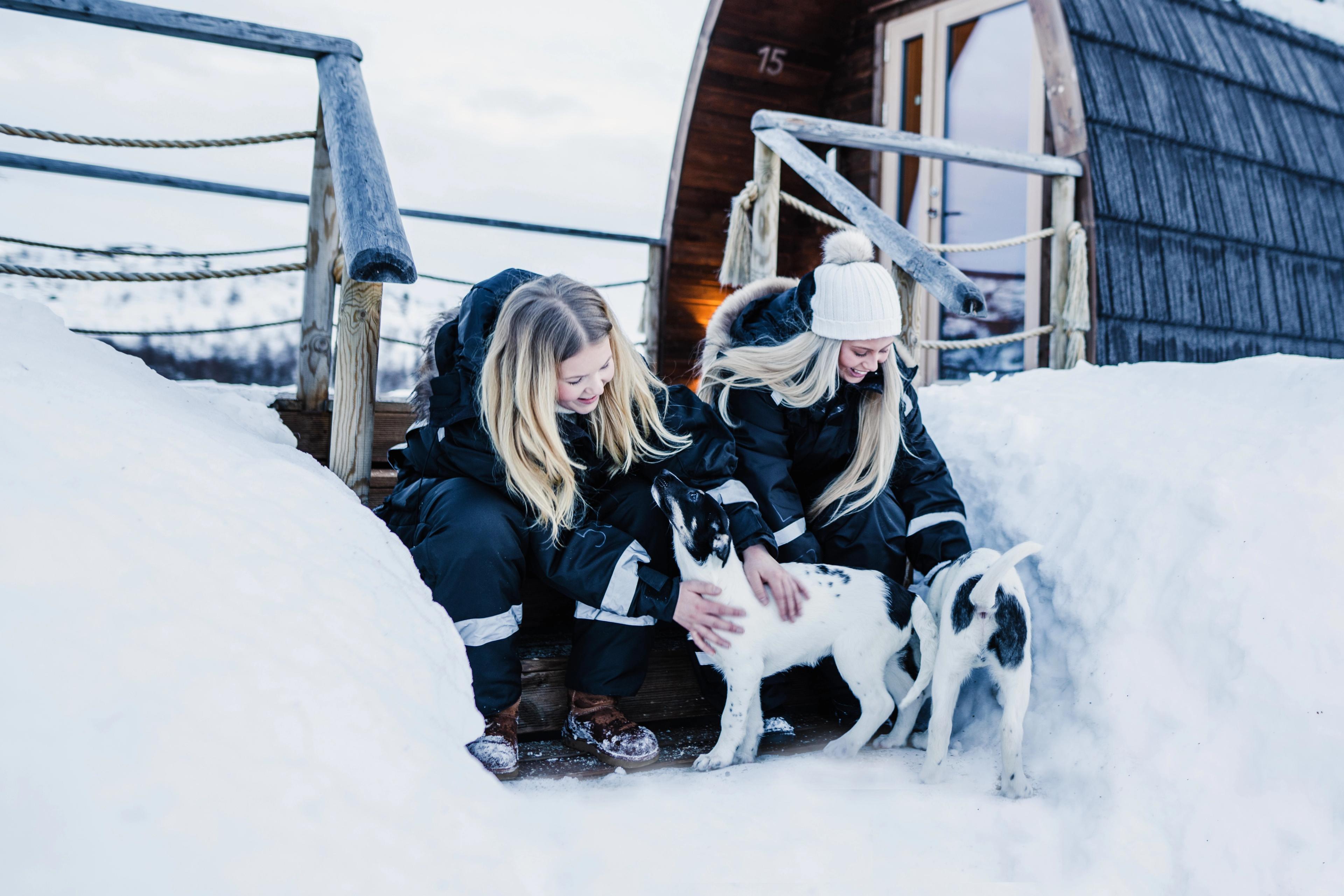 Two girls clapping husky puppies outside Snowhotel Kirkenes