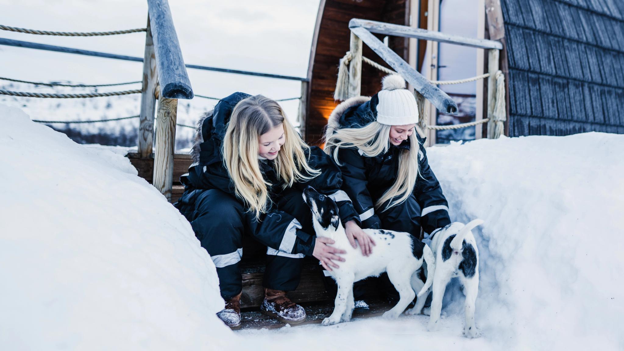 Two girls clapping husky puppies outside Snowhotel Kirkenes