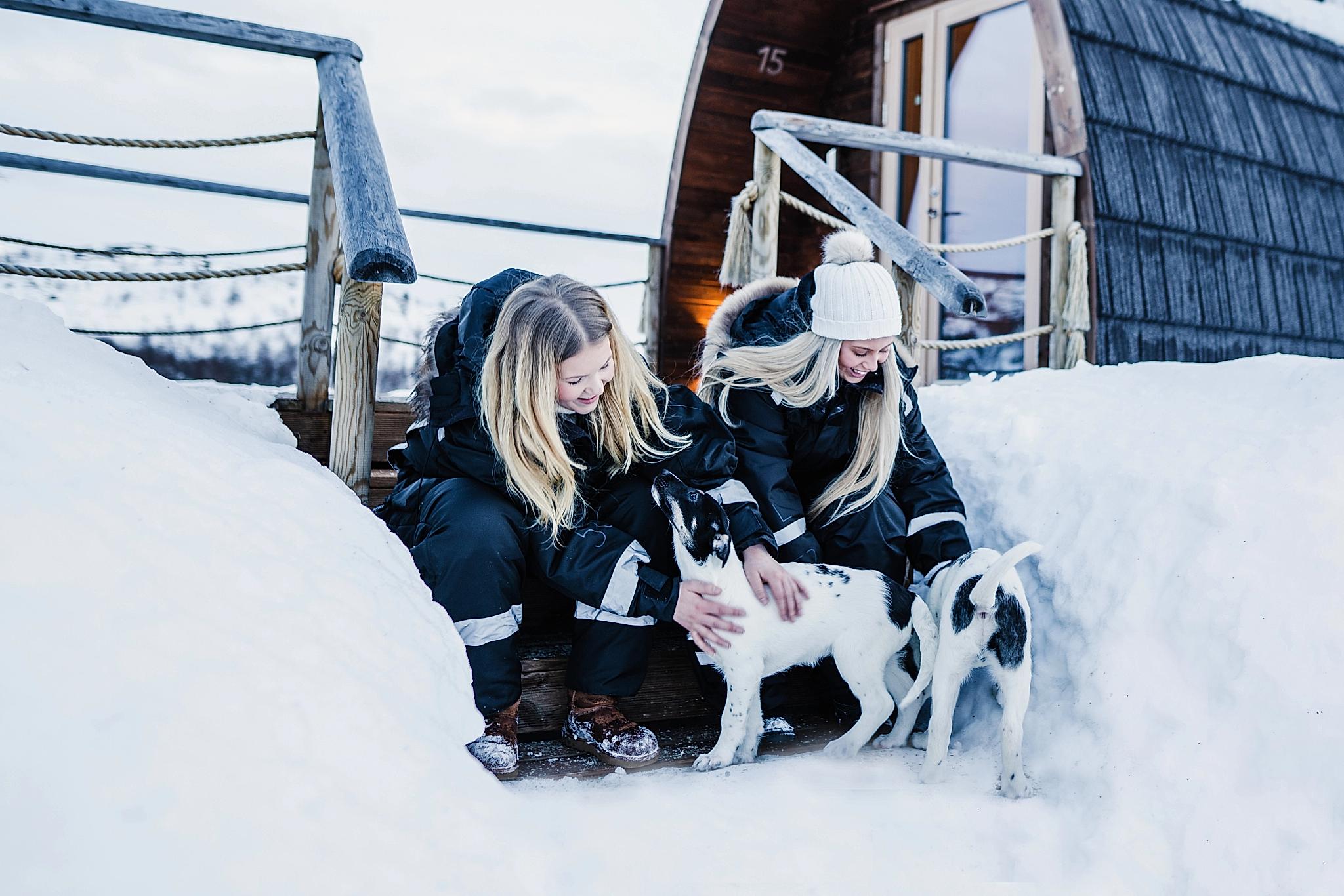 Two girls clapping husky puppies outside Snowhotel Kirkenes
