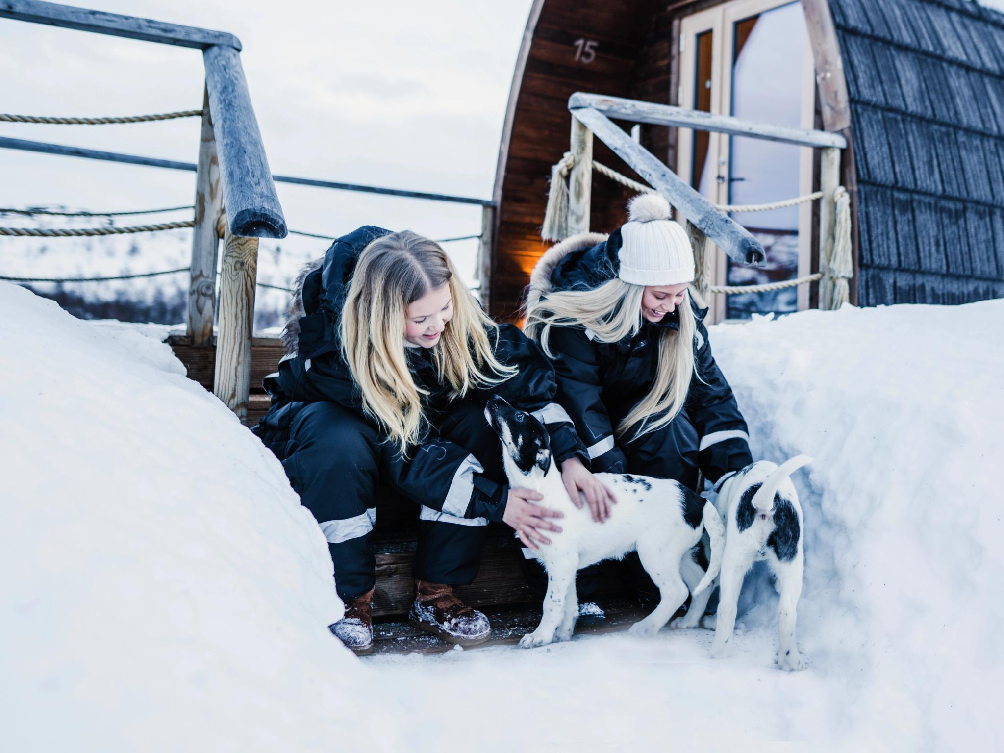 Two girls clapping husky puppies outside Snowhotel Kirkenes