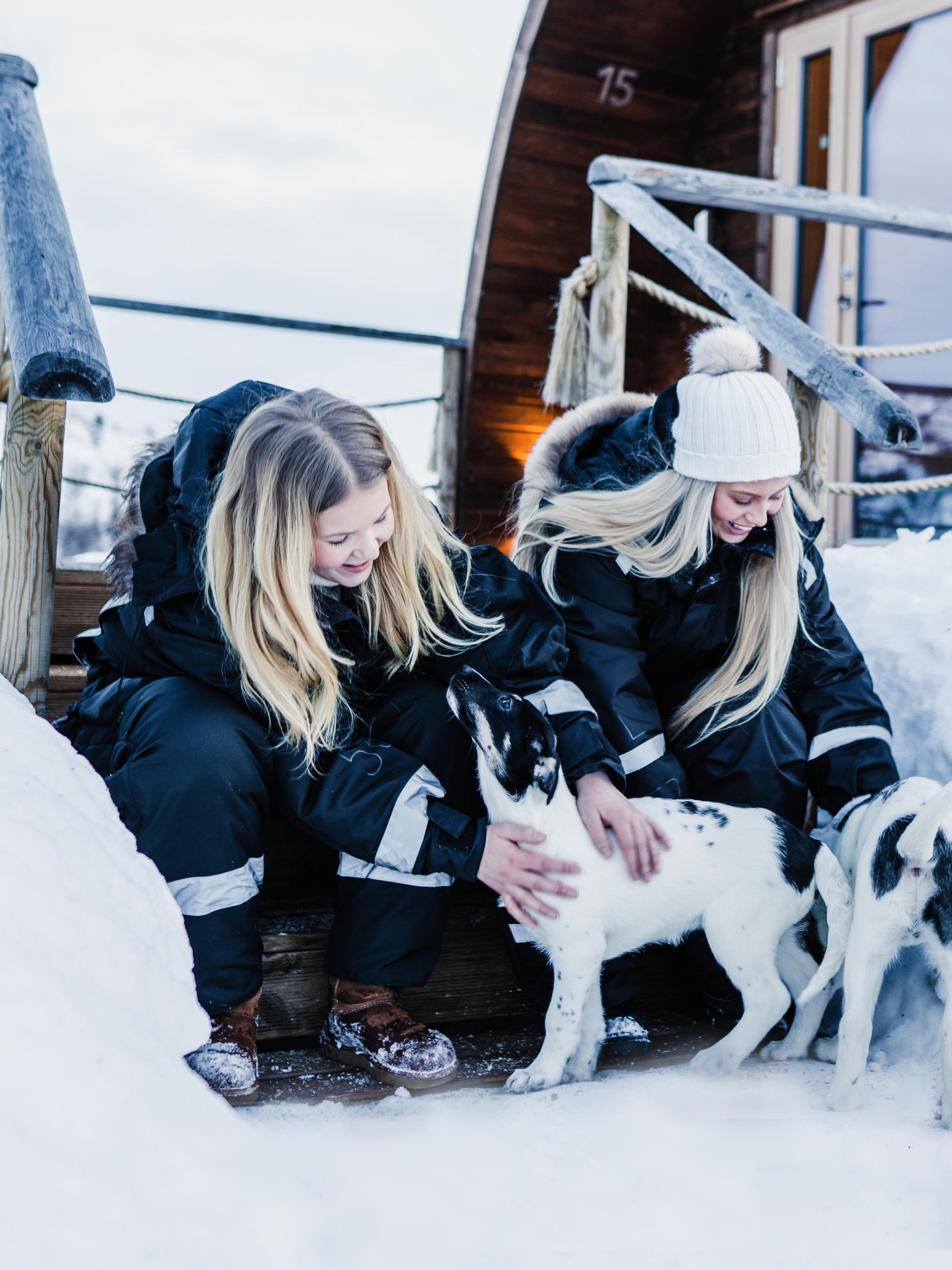 Two girls clapping husky puppies outside Snowhotel Kirkenes