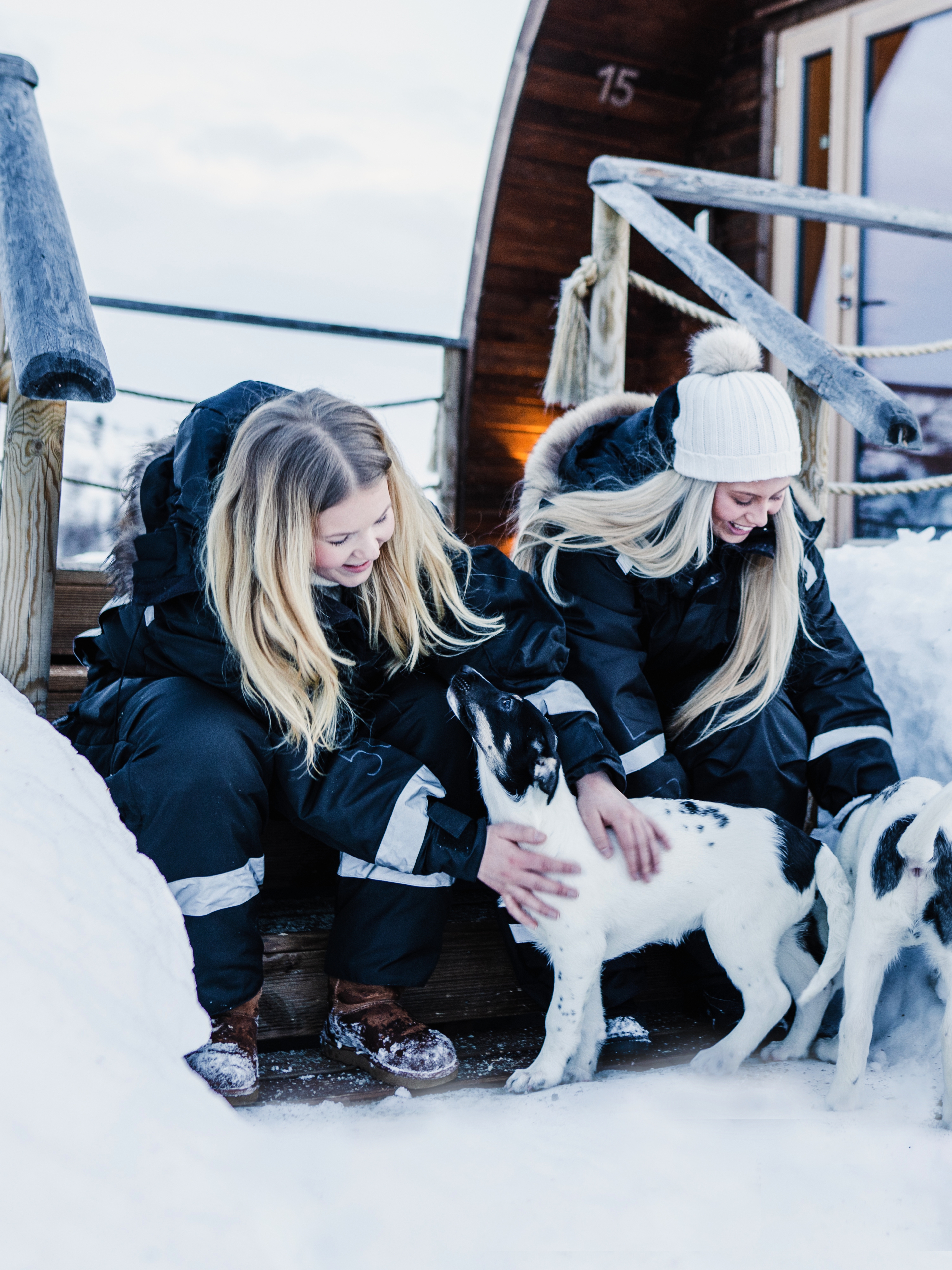 Two girls clapping husky puppies outside Snowhotel Kirkenes