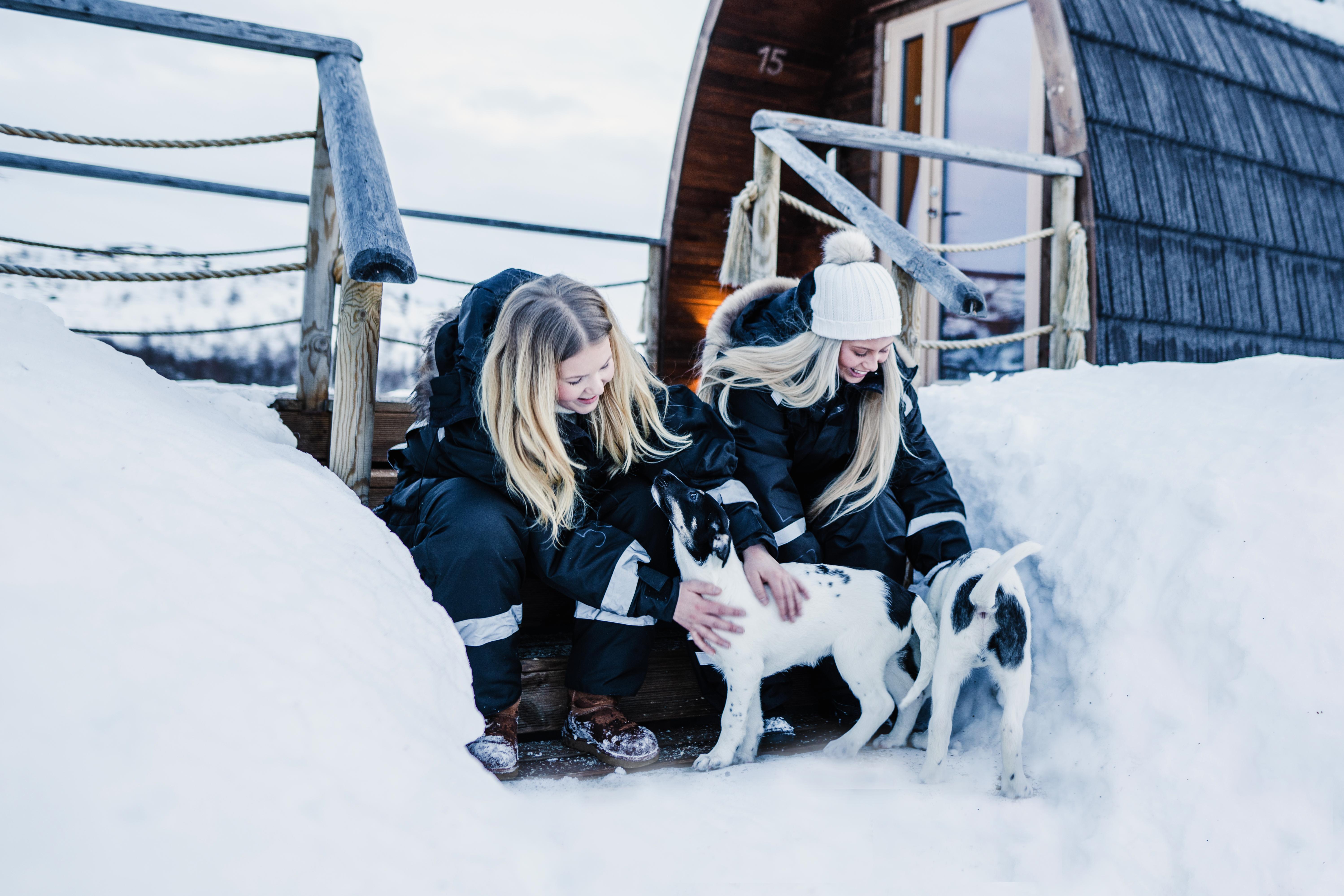 Two girls clapping husky puppies outside Snowhotel Kirkenes