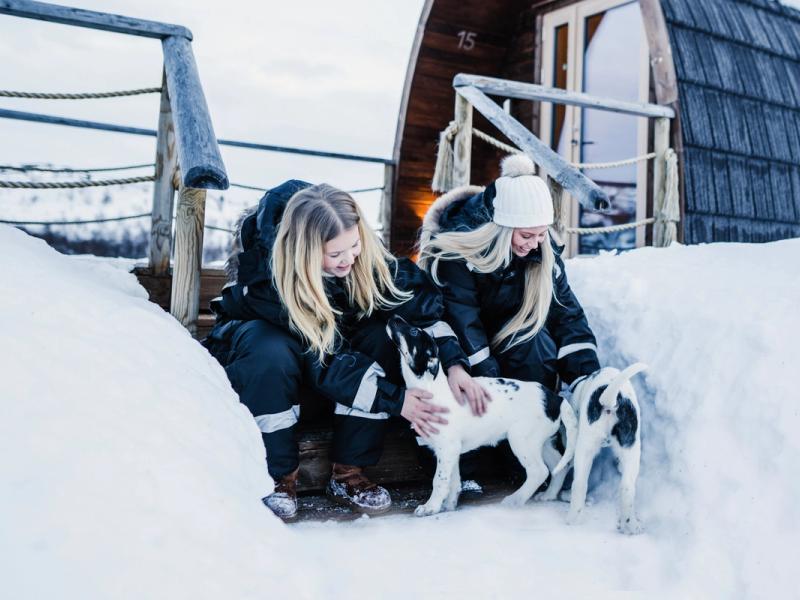Two girls clapping husky puppies outside Snowhotel Kirkenes