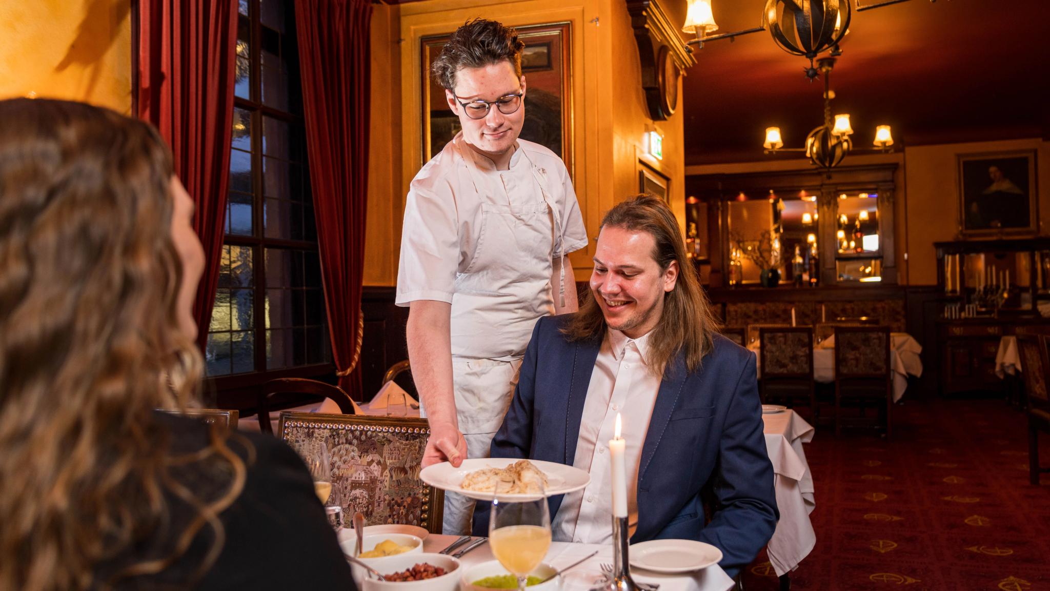 A man and a woman being served lutefisk by chef at Gamle Raadhus Restaurant in Oslo