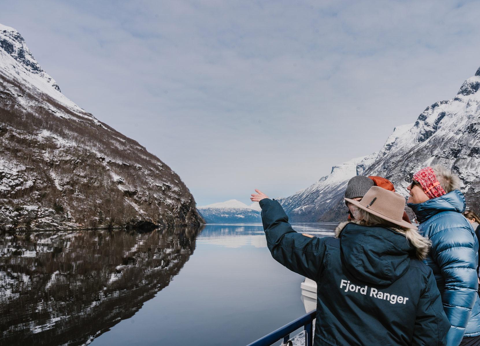 Three people pointing at a mountain while on a wintercruise in Geirangerfjorden, Sunnmøre.