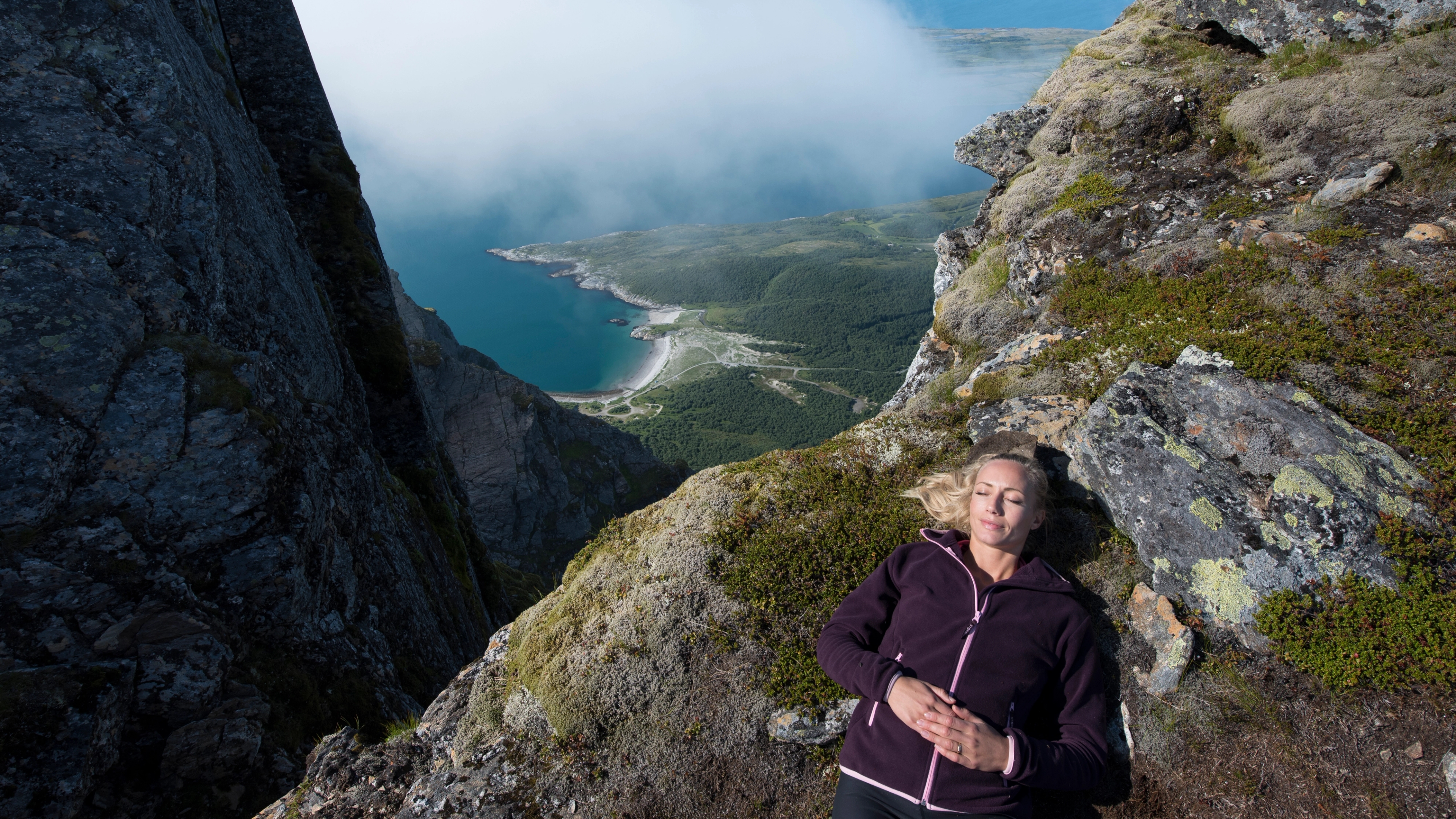 A hiker lying down for a rest on the way to the top of Dønnamannen in Helgeland, Northern Norway. In the background, there is the ocean.