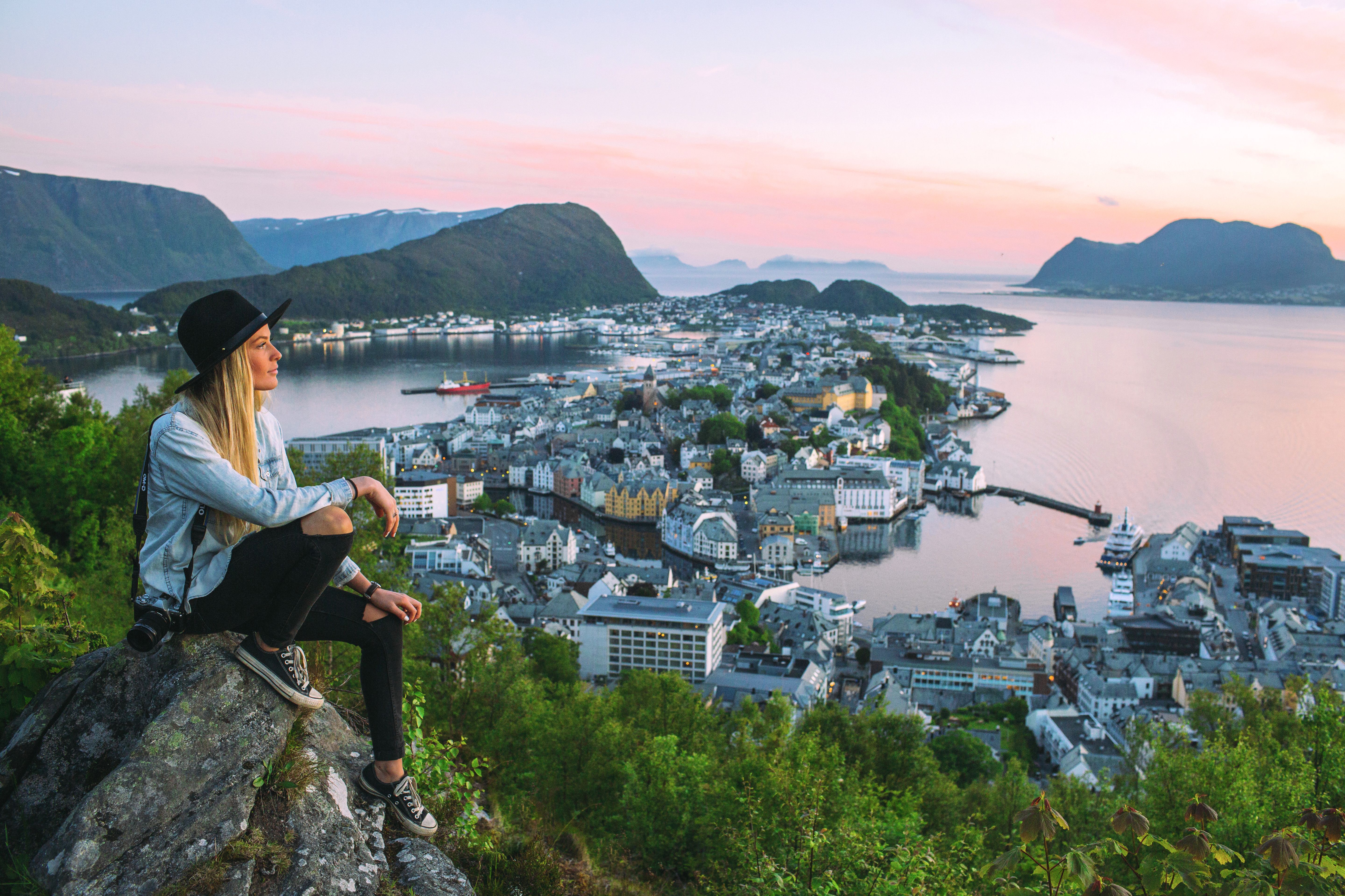 Woman sitting at the top of Aksla mountain in Ålesund city with a pink sunset, Fjord Norway