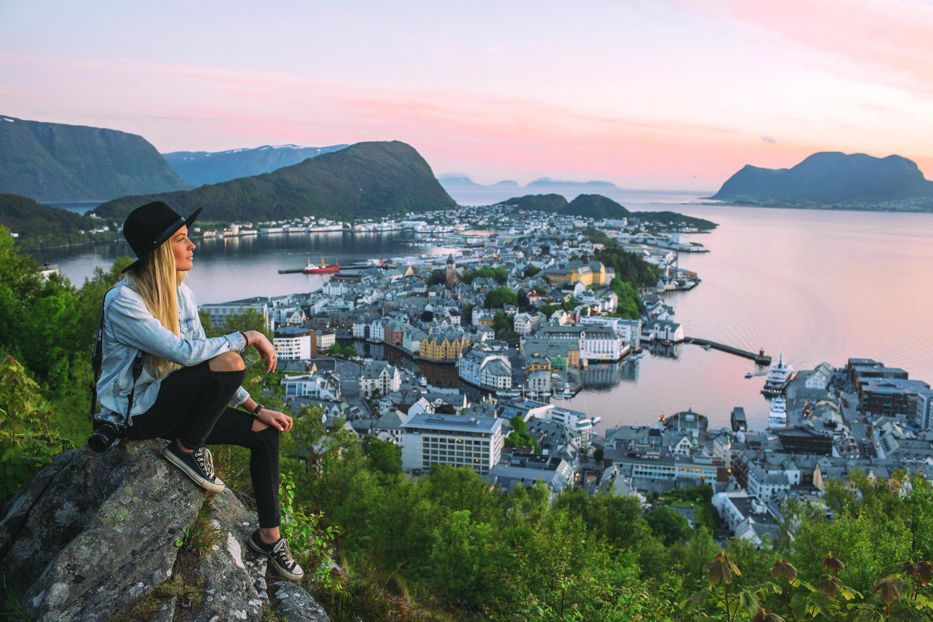 Woman sitting at the top of Aksla mountain in Ålesund city with a pink sunset, Fjord Norway