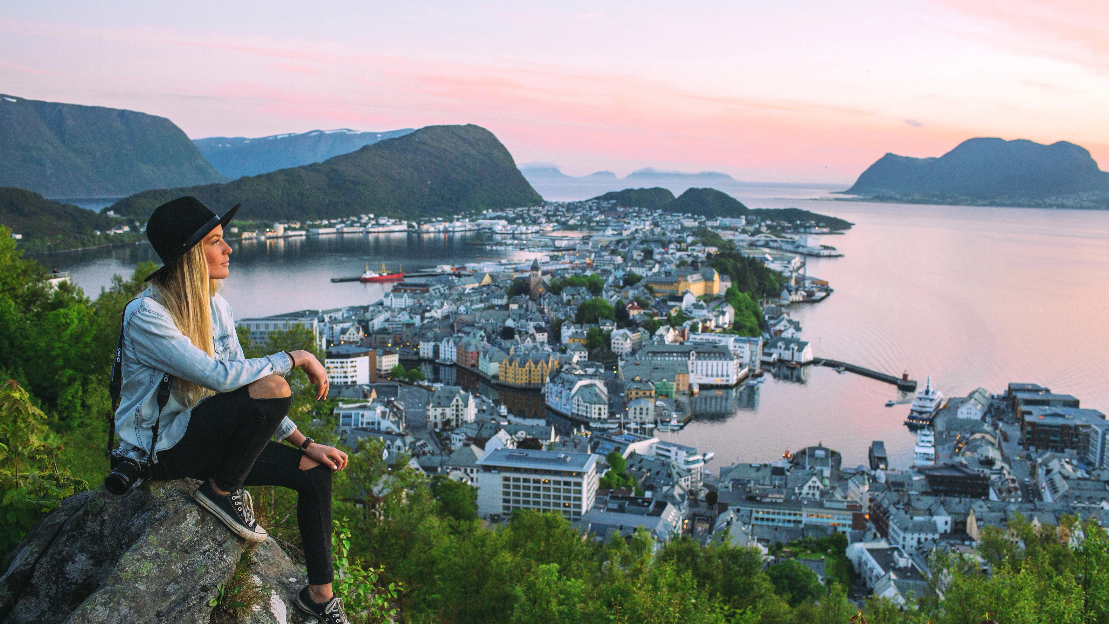 Woman sitting at the top of Aksla mountain in Ålesund city with a pink sunset, Fjord Norway