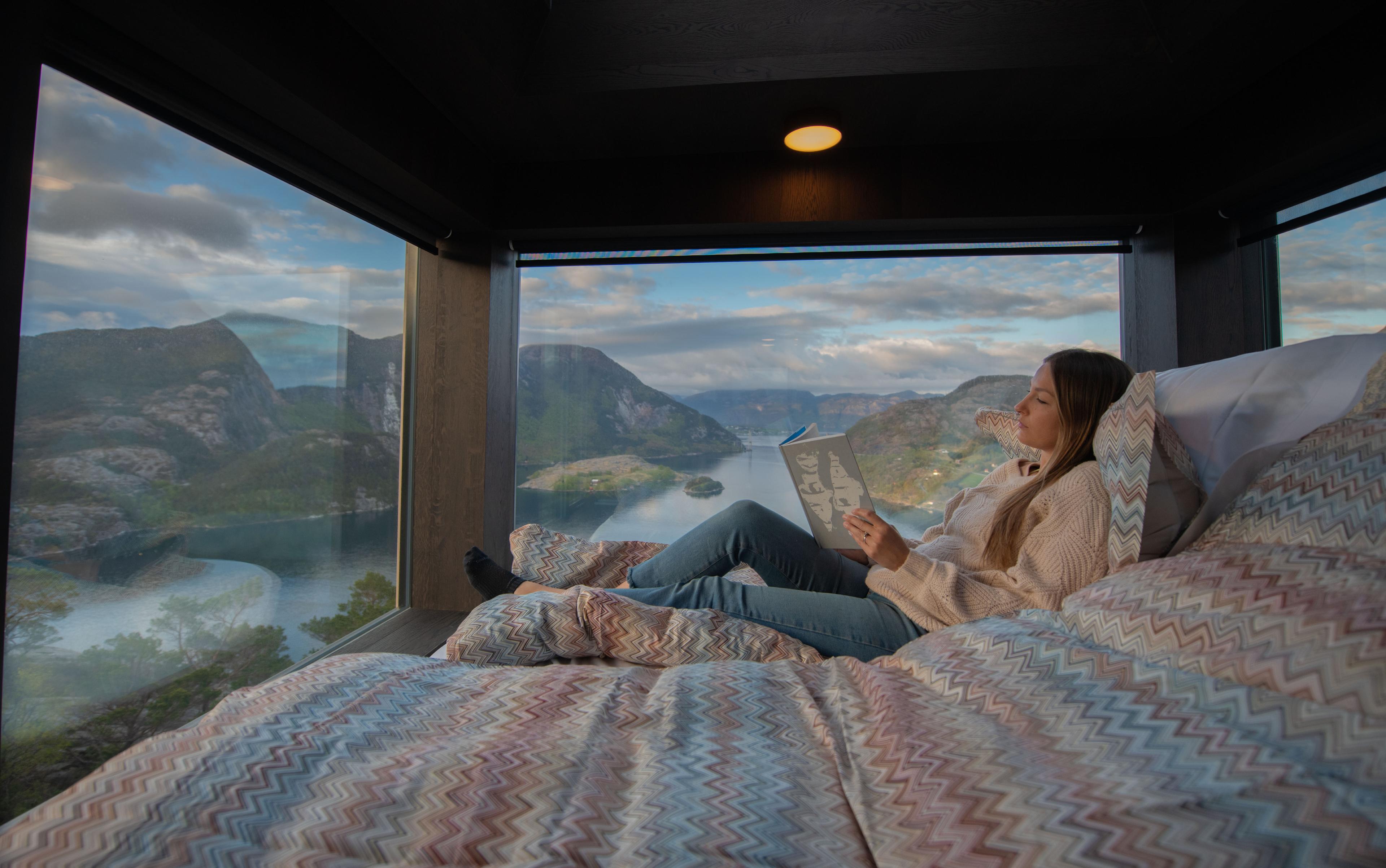 A woman reading in a bed inside a sky lodge at The Bolder in Rogaland, Fjord Norway