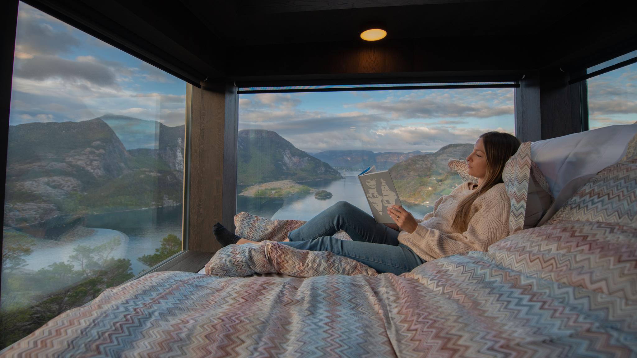 A woman reading in a bed inside a sky lodge at The Bolder in Rogaland, Fjord Norway