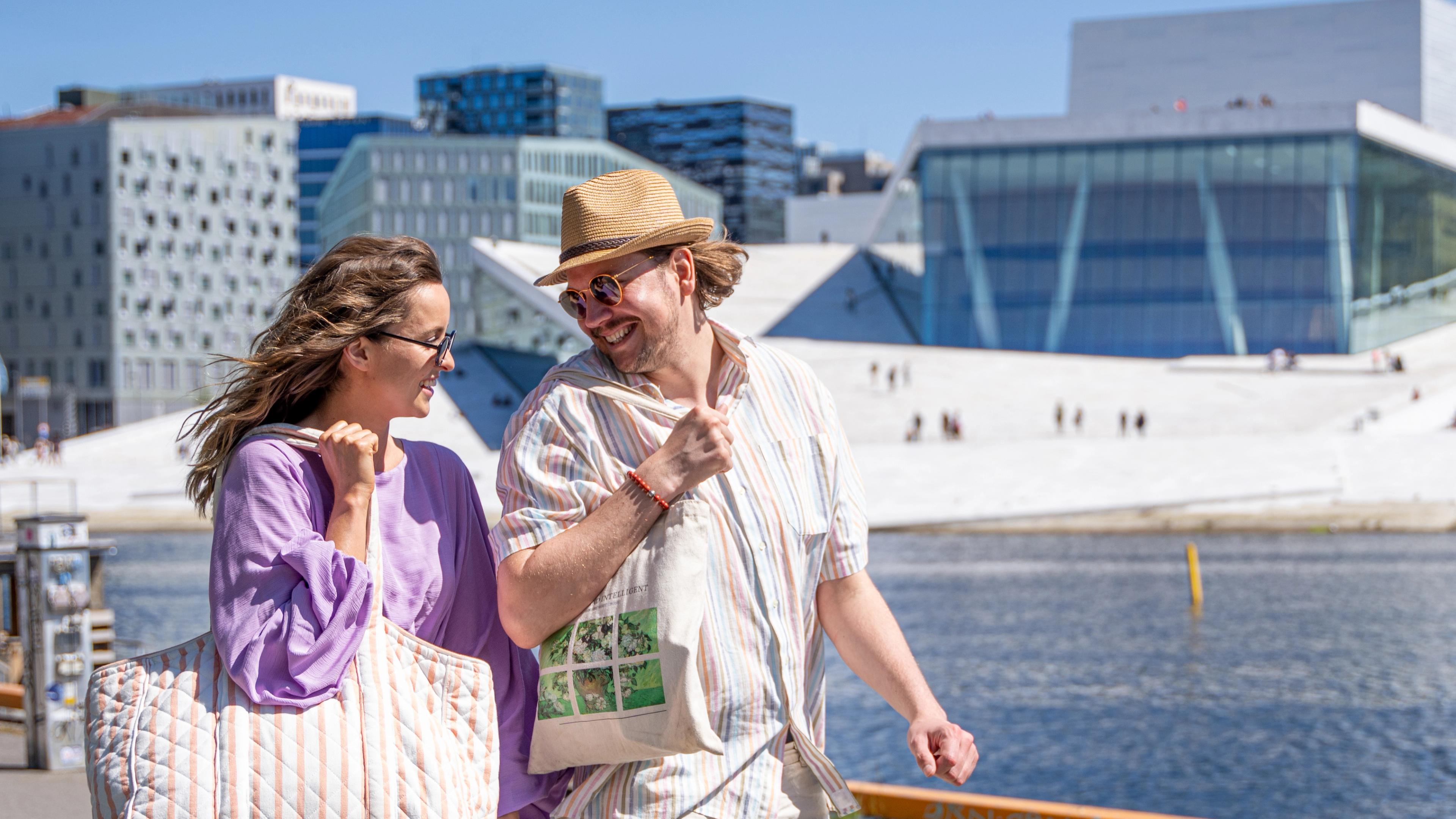 Man and woman walking the Oslo harbour promenade, the Opera house in the back