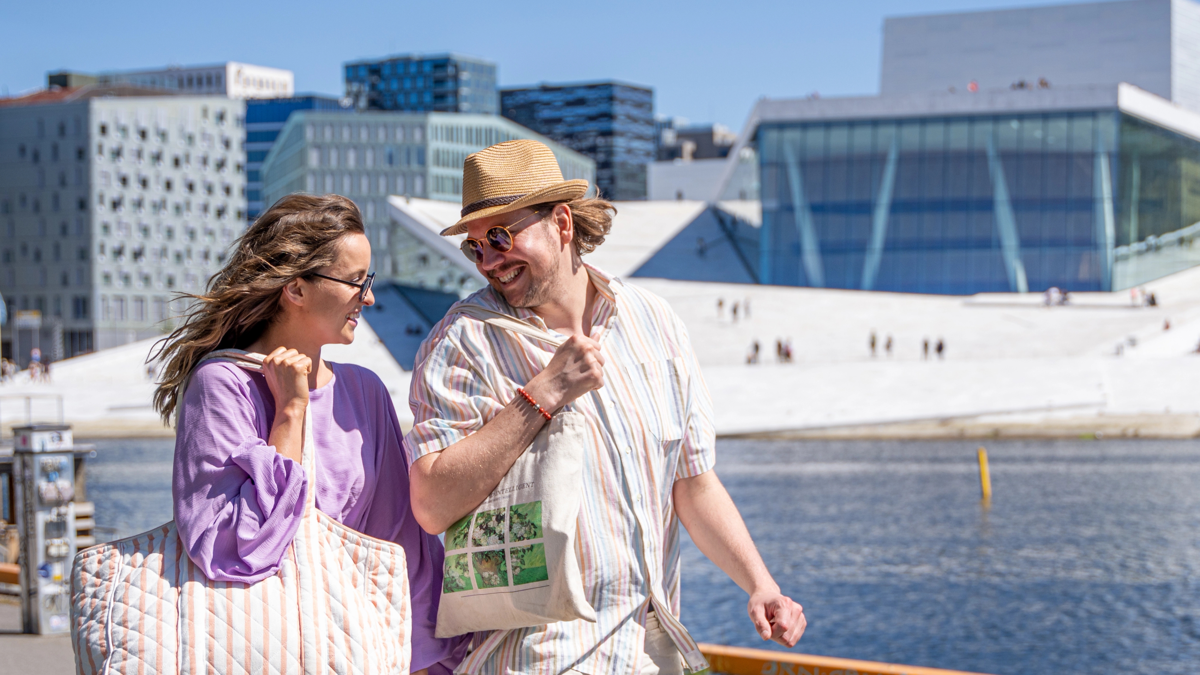 Man and woman walking the Oslo harbour promenade, the Opera house in the back