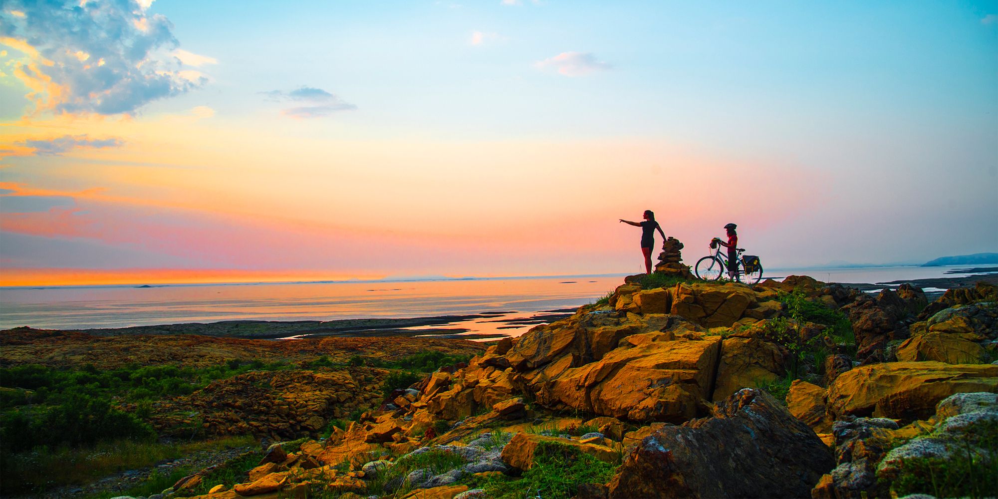 A hiker and a cyclist standing side by side watching the sunset at the Leka island in Trøndelag.