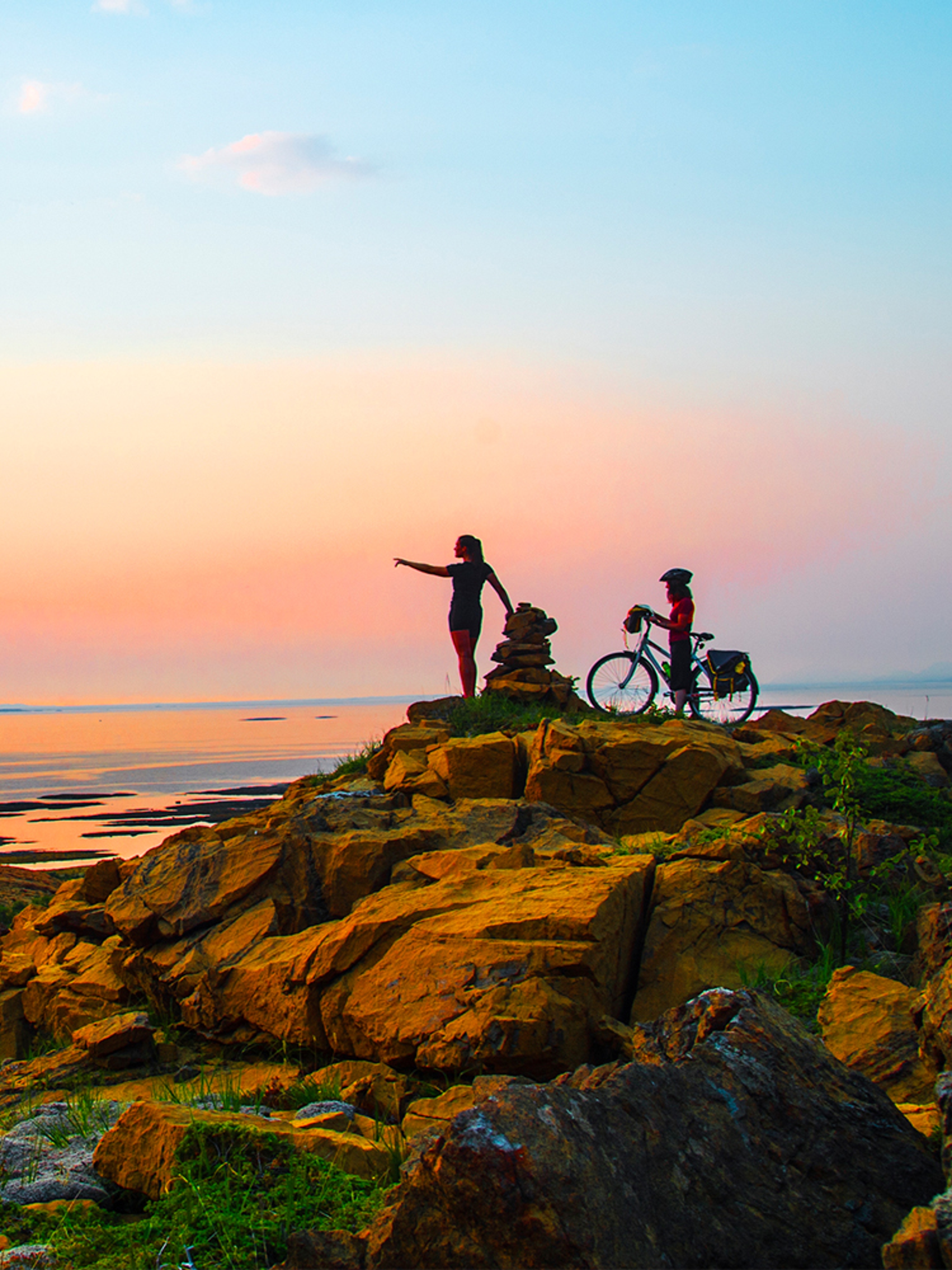 A hiker and a cyclist standing side by side watching the sunset at the Leka island in Trøndelag.