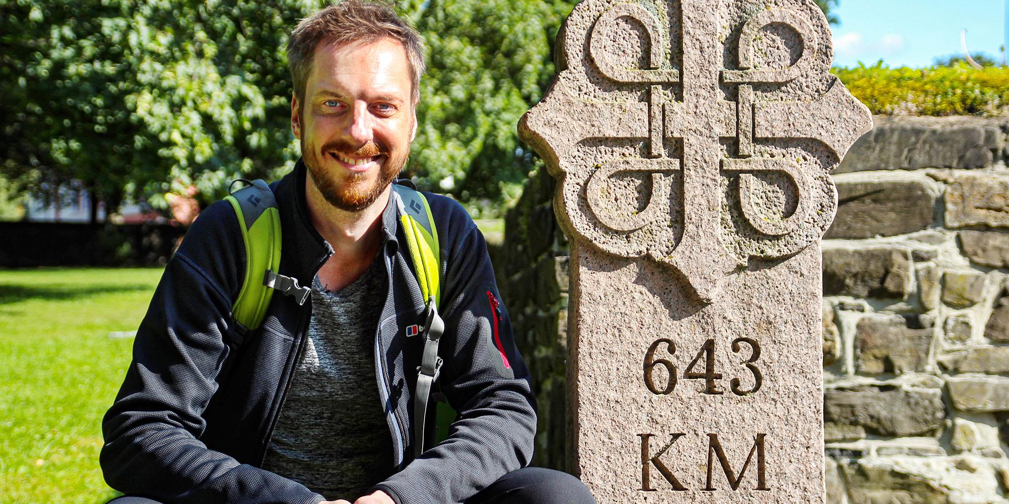 Pilgrim Kes Blans next to a sign that marks the start of the St. Olav Ways pilgrim path from Oslo to Trondheim, Norway