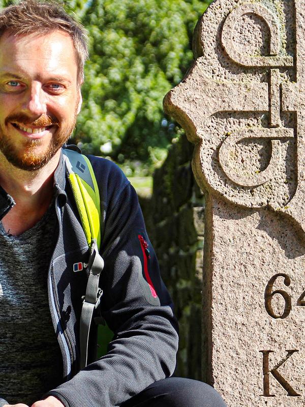 Pilgrim Kes Blans next to a sign that marks the start of the St. Olav Ways pilgrim path from Oslo to Trondheim, Norway