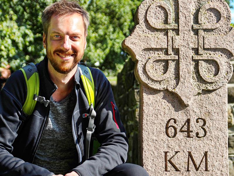 Pilgrim Kes Blans next to a sign that marks the start of the St. Olav Ways pilgrim path from Oslo to Trondheim, Norway