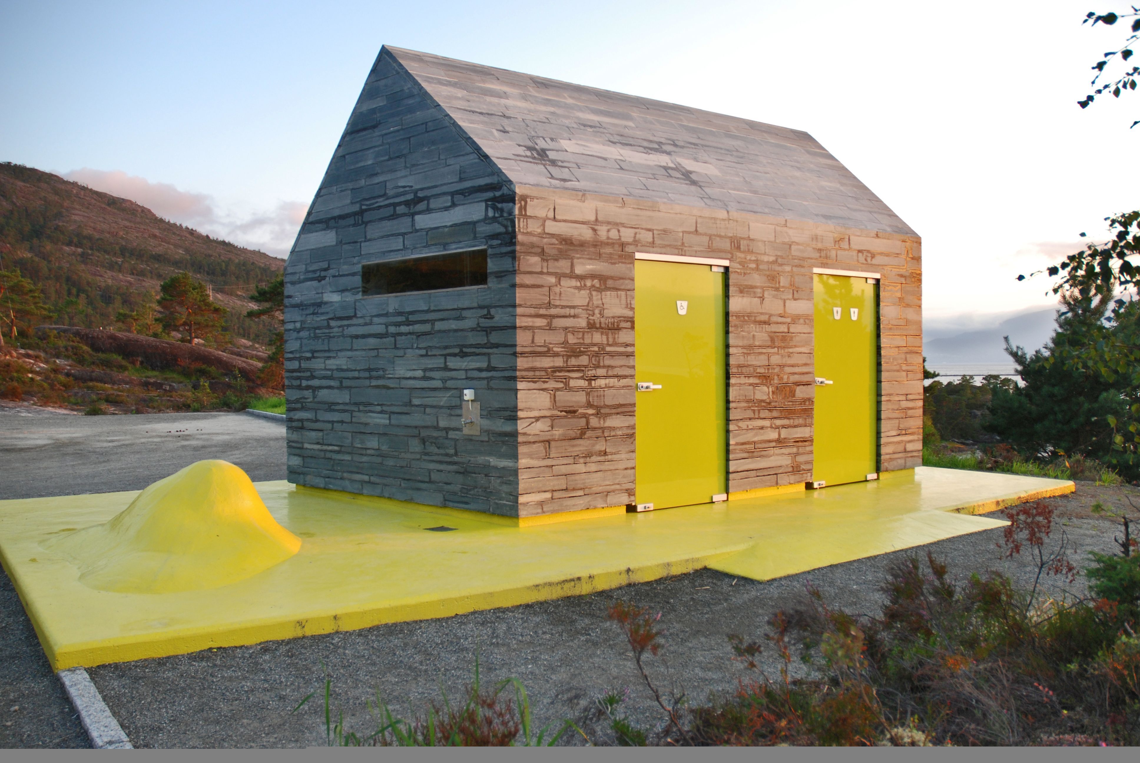 A grey and yellow toilet building in nature.