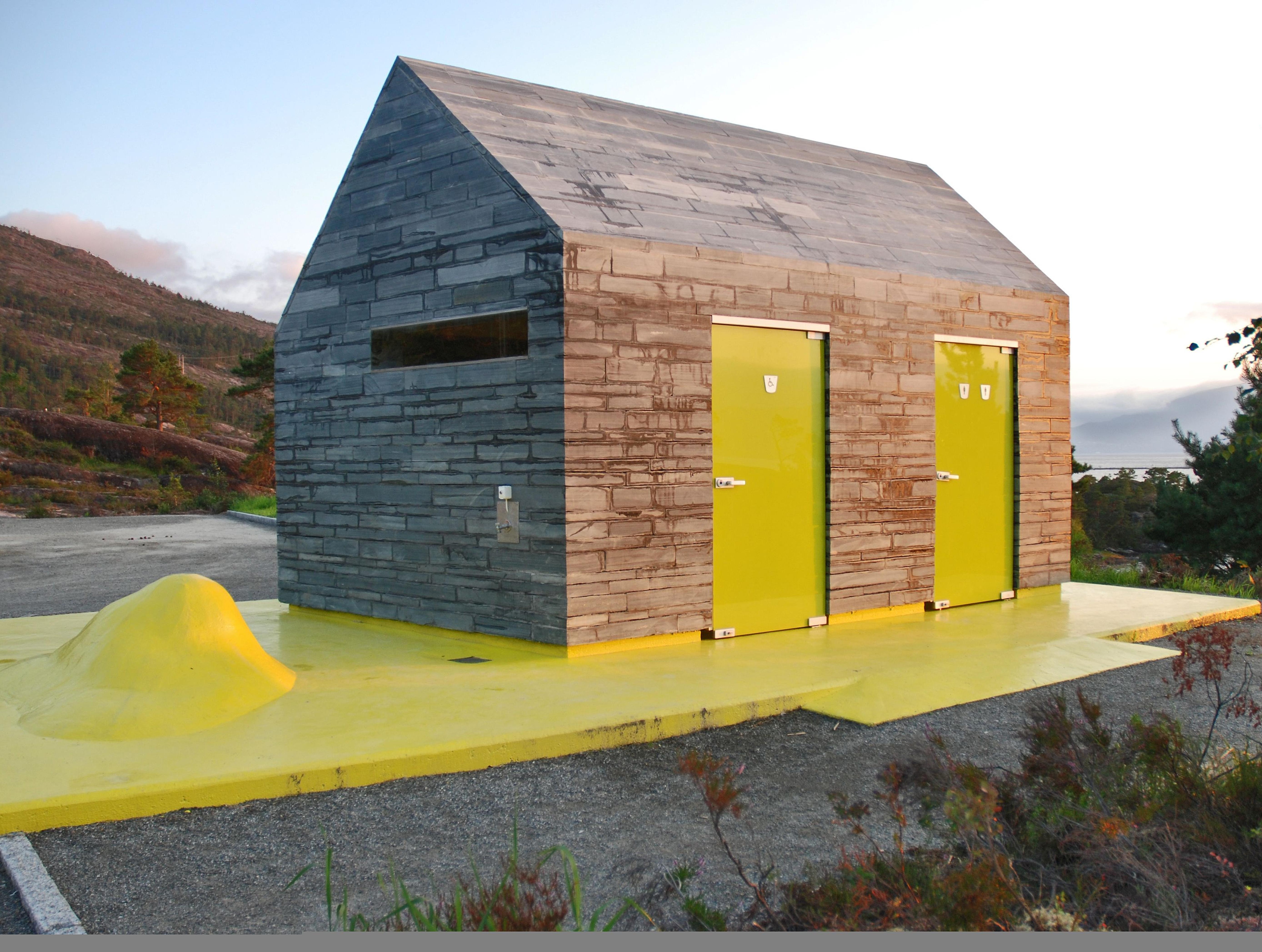 A grey and yellow toilet building in nature.