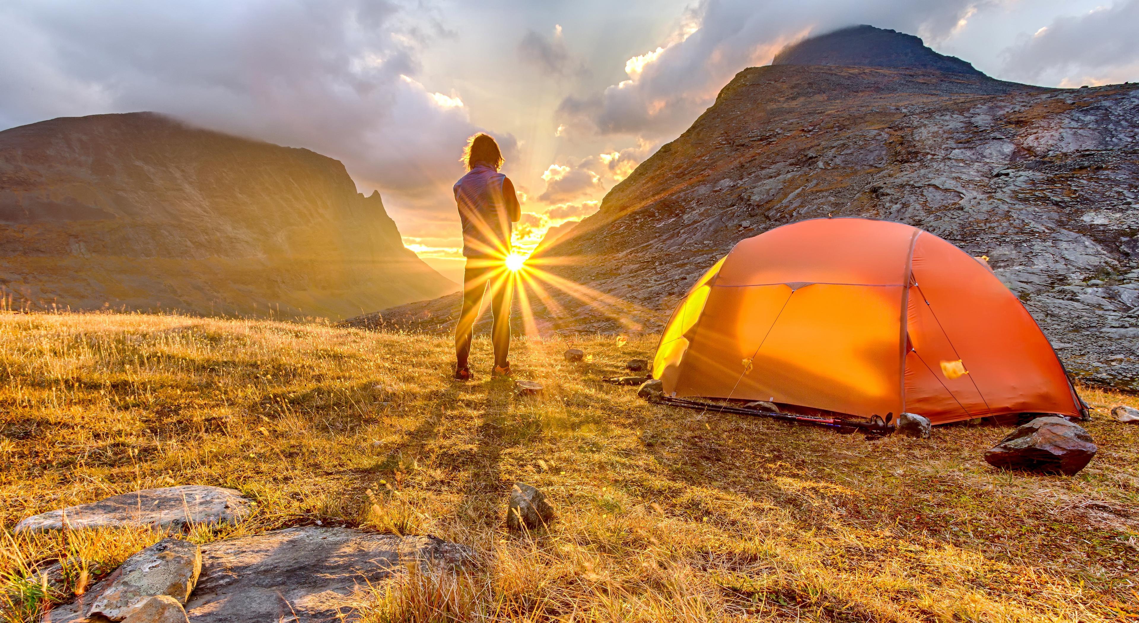 Person står foran telt og ser på solnedgangen i Hardangervidda nasjonalpark
