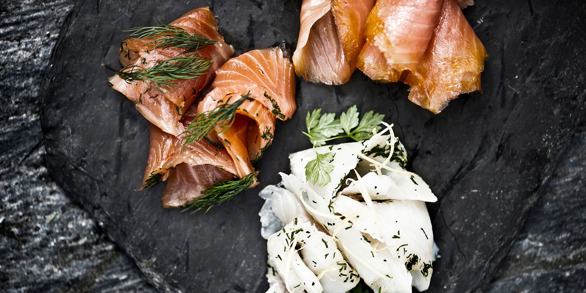 A stone platter with smoked salmon and other food
