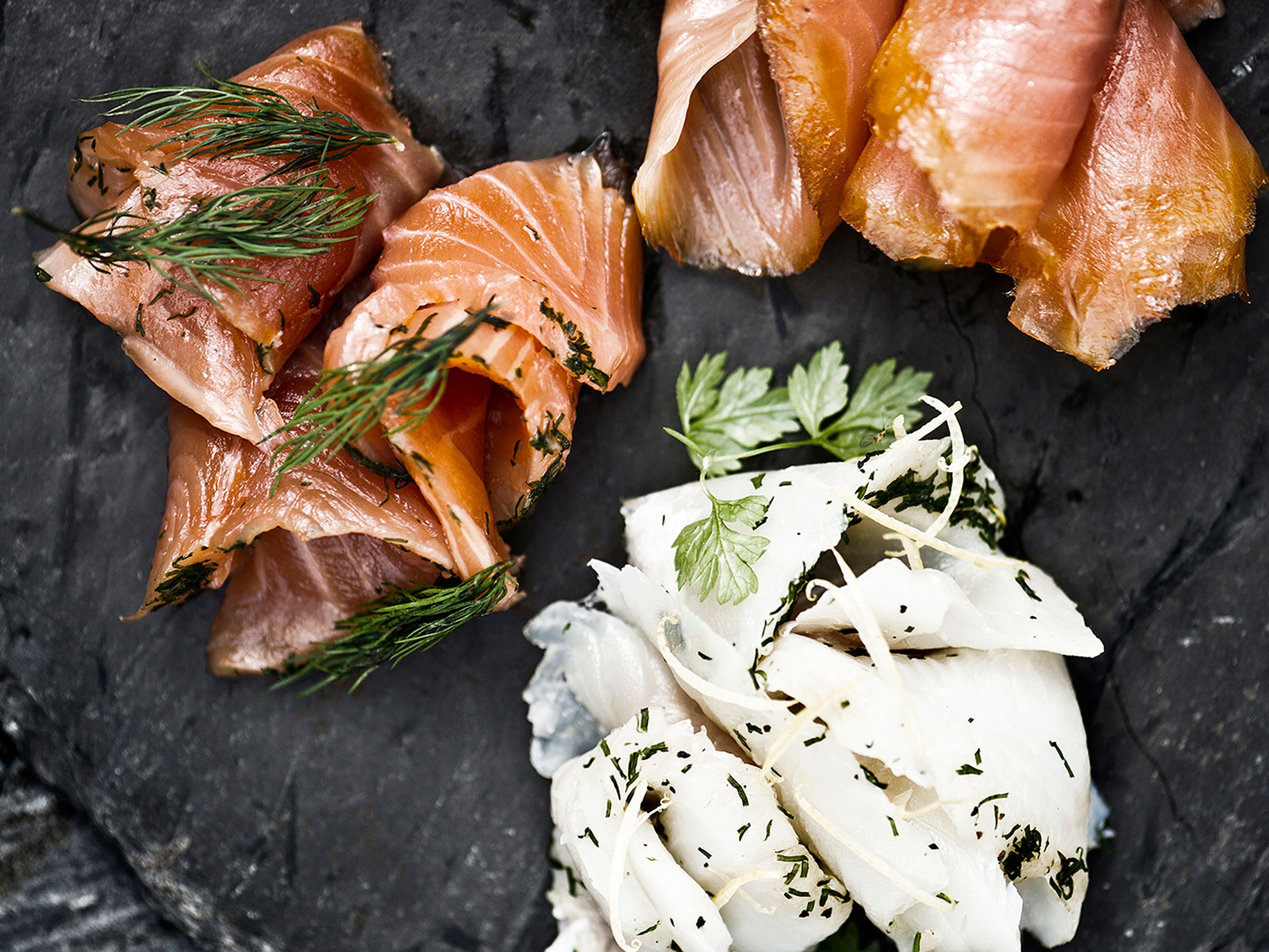 A stone platter with smoked salmon and other food