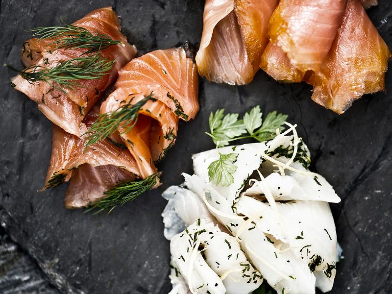 A stone platter with smoked salmon and other food