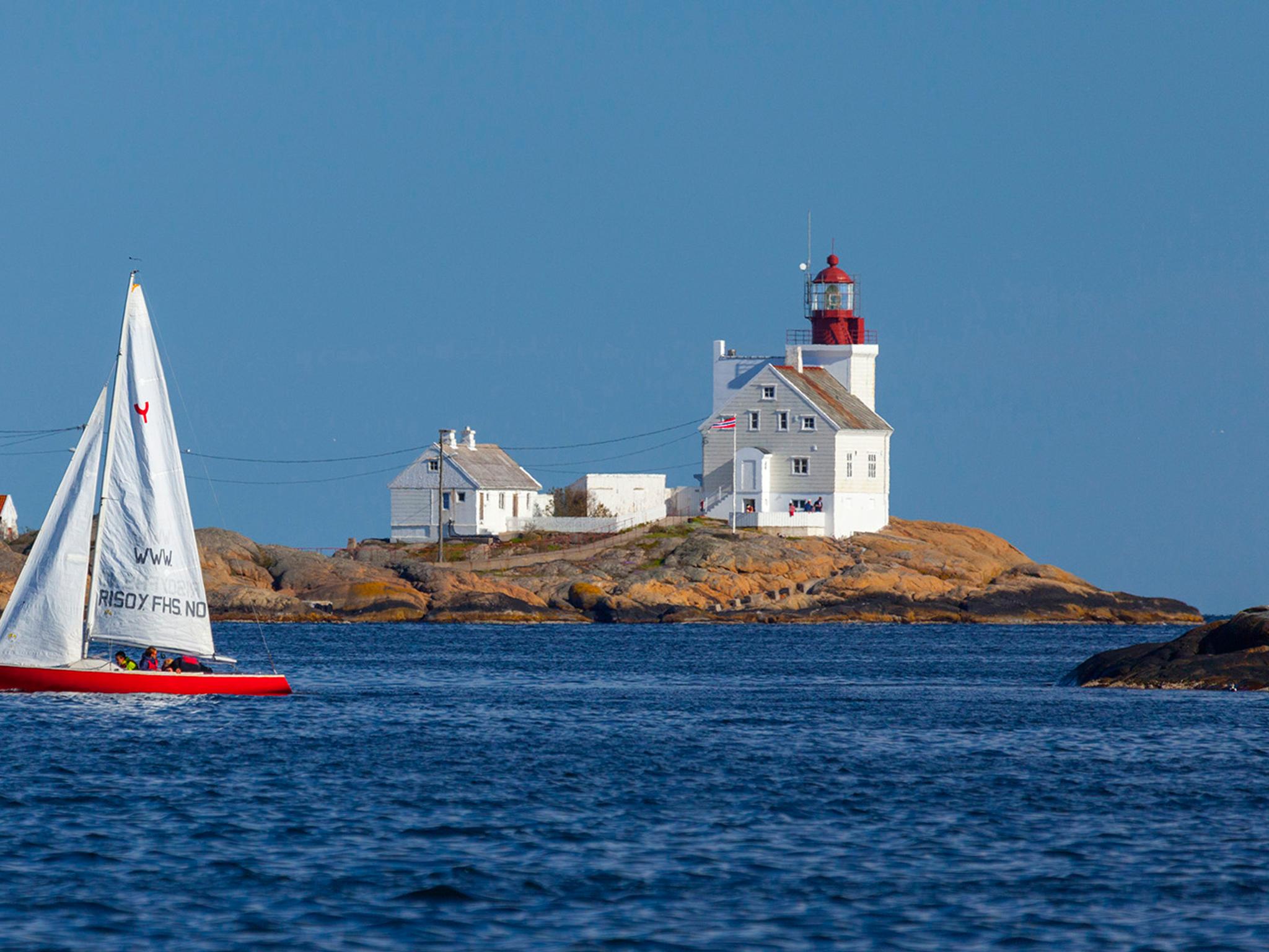 A sailboat passing by the Lyngør lighthouse during summer in Southern Norway.
