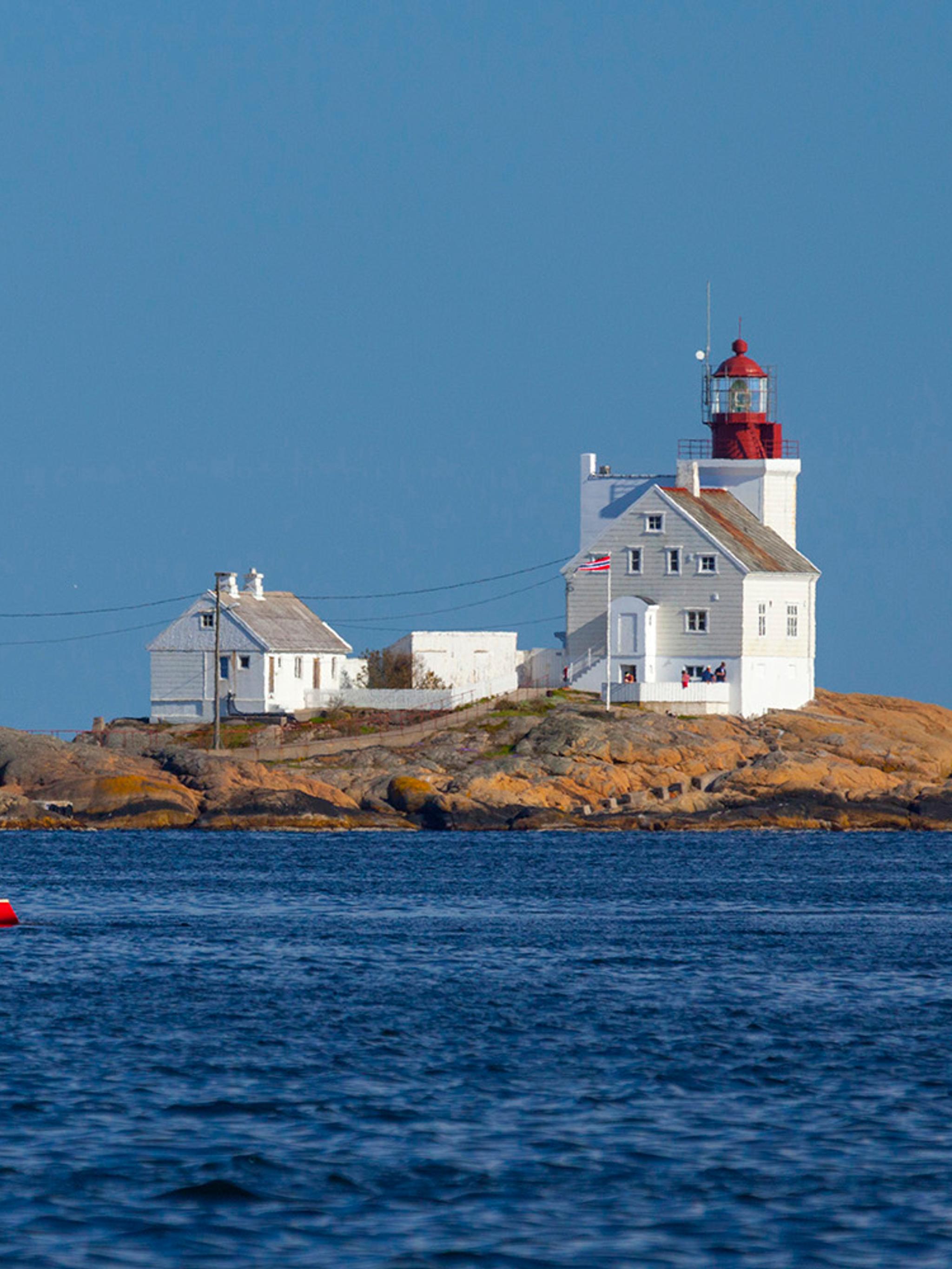 A sailboat passing by the Lyngør lighthouse during summer in Southern Norway.