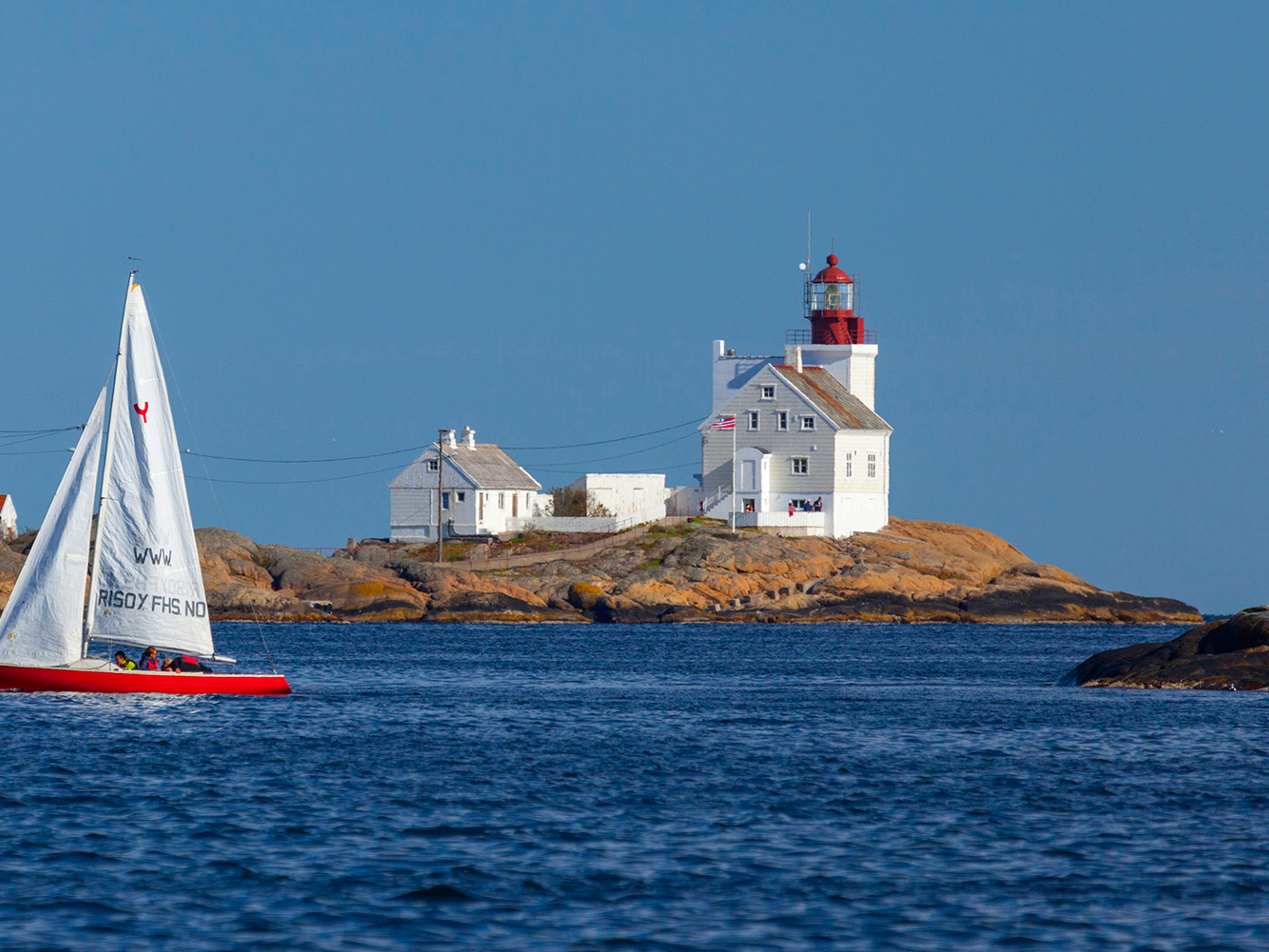 A sailboat passing by the Lyngør lighthouse during summer in Southern Norway.
