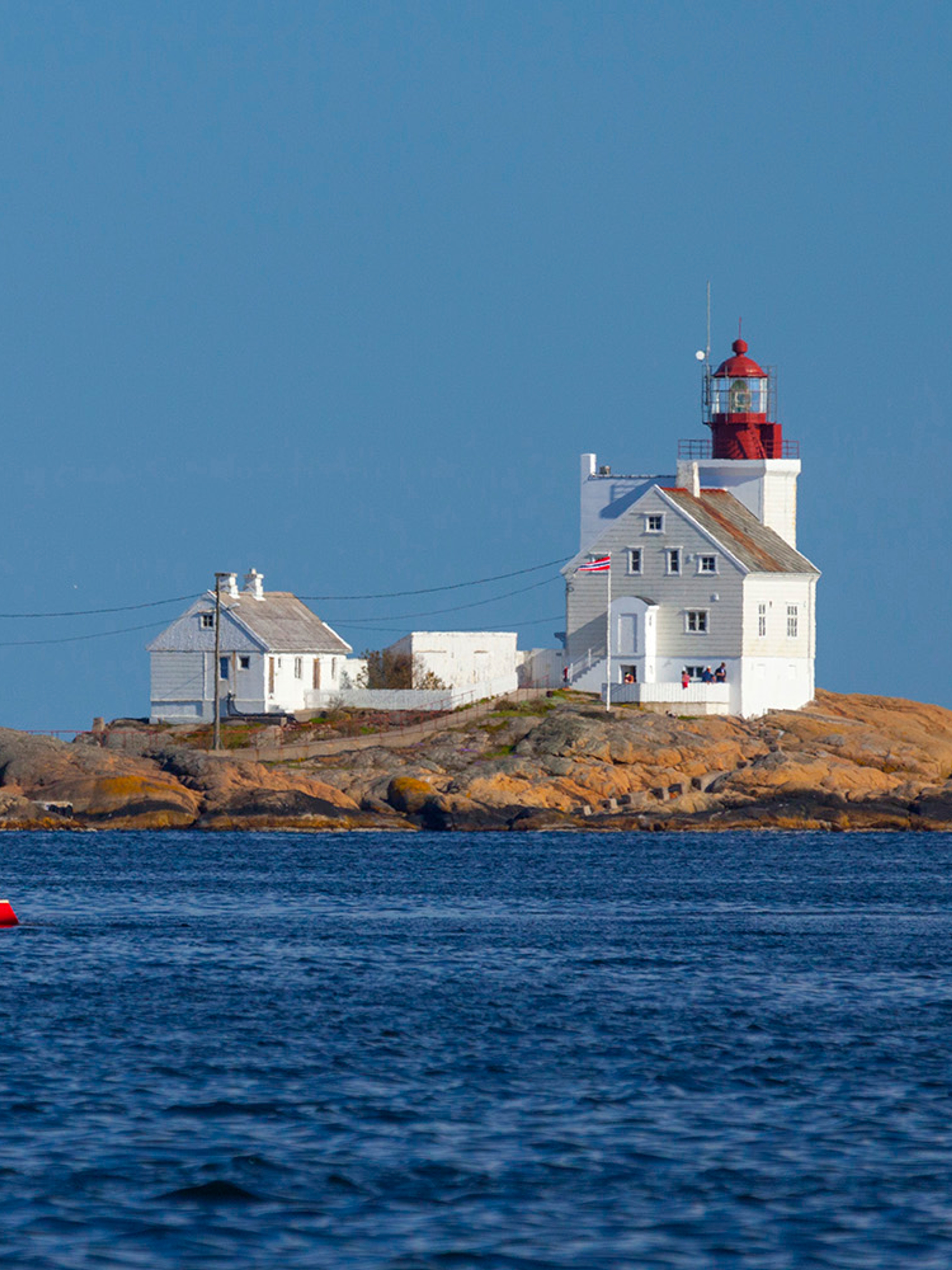 A sailboat passing by the Lyngør lighthouse during summer in Southern Norway.