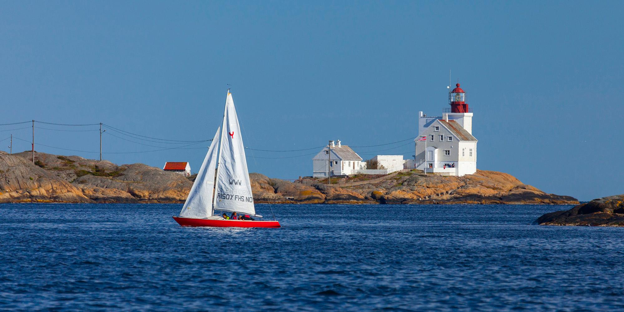 A sailboat passing by the Lyngør lighthouse during summer in Southern Norway.