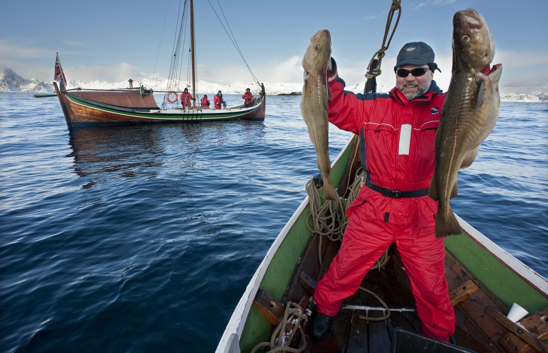 En man håller upp två stora torskar på en båt utanför Bodø i norra Norge