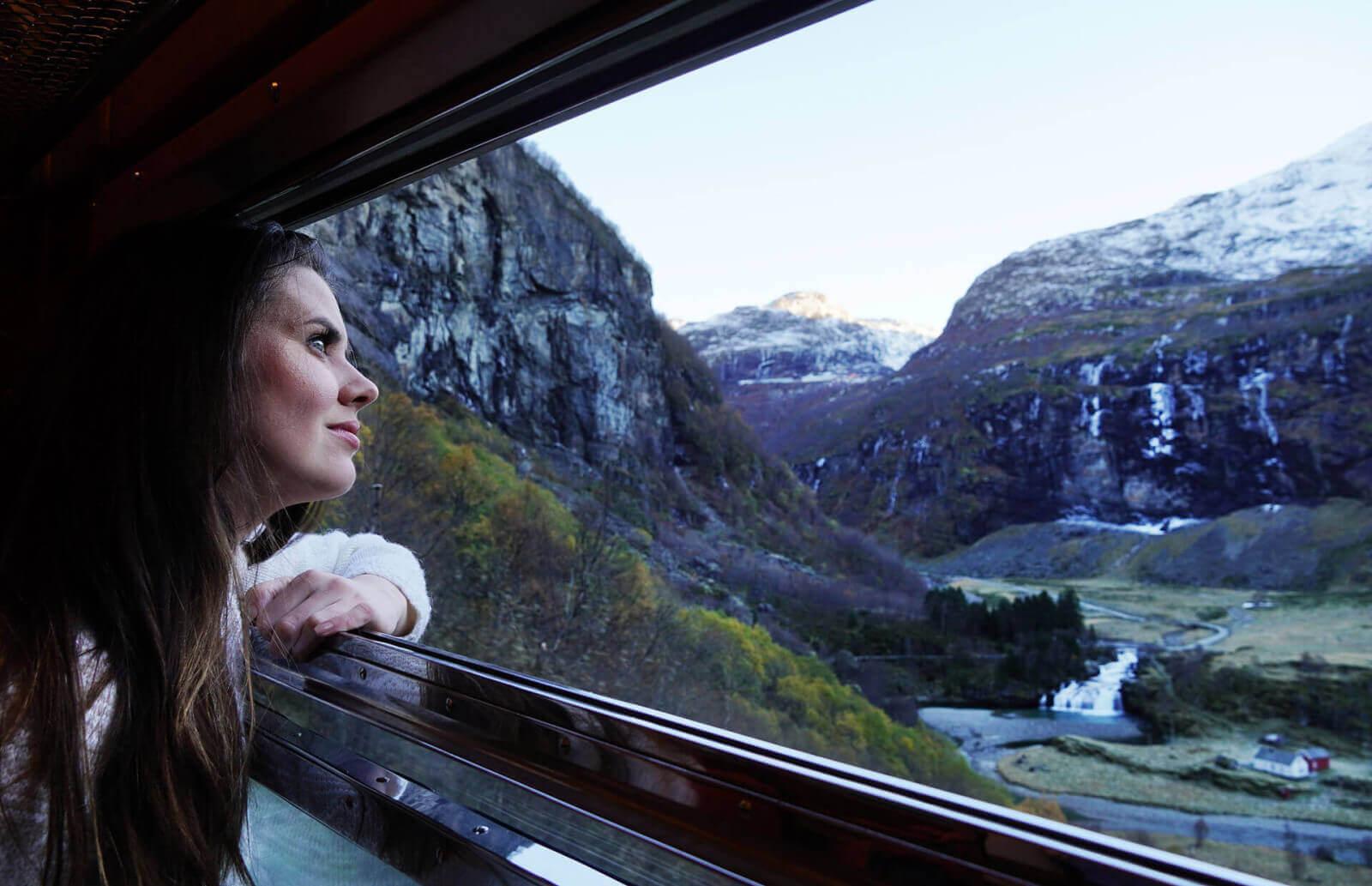 Woman gazes at mountains and waterfalls from train window.