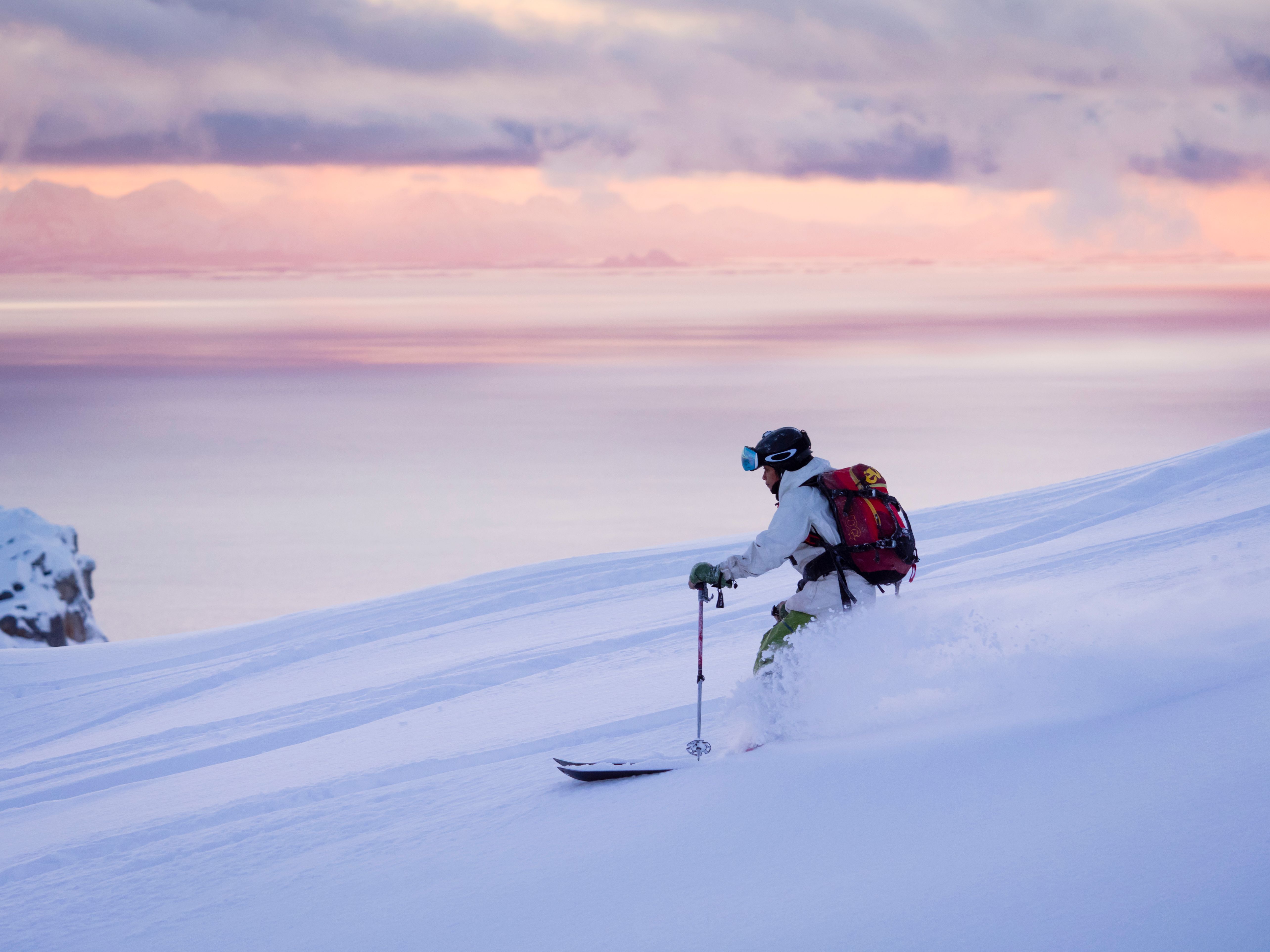 Woman skiing at Småtindan mountain under a pink sky in Lofoten, Northern Norway