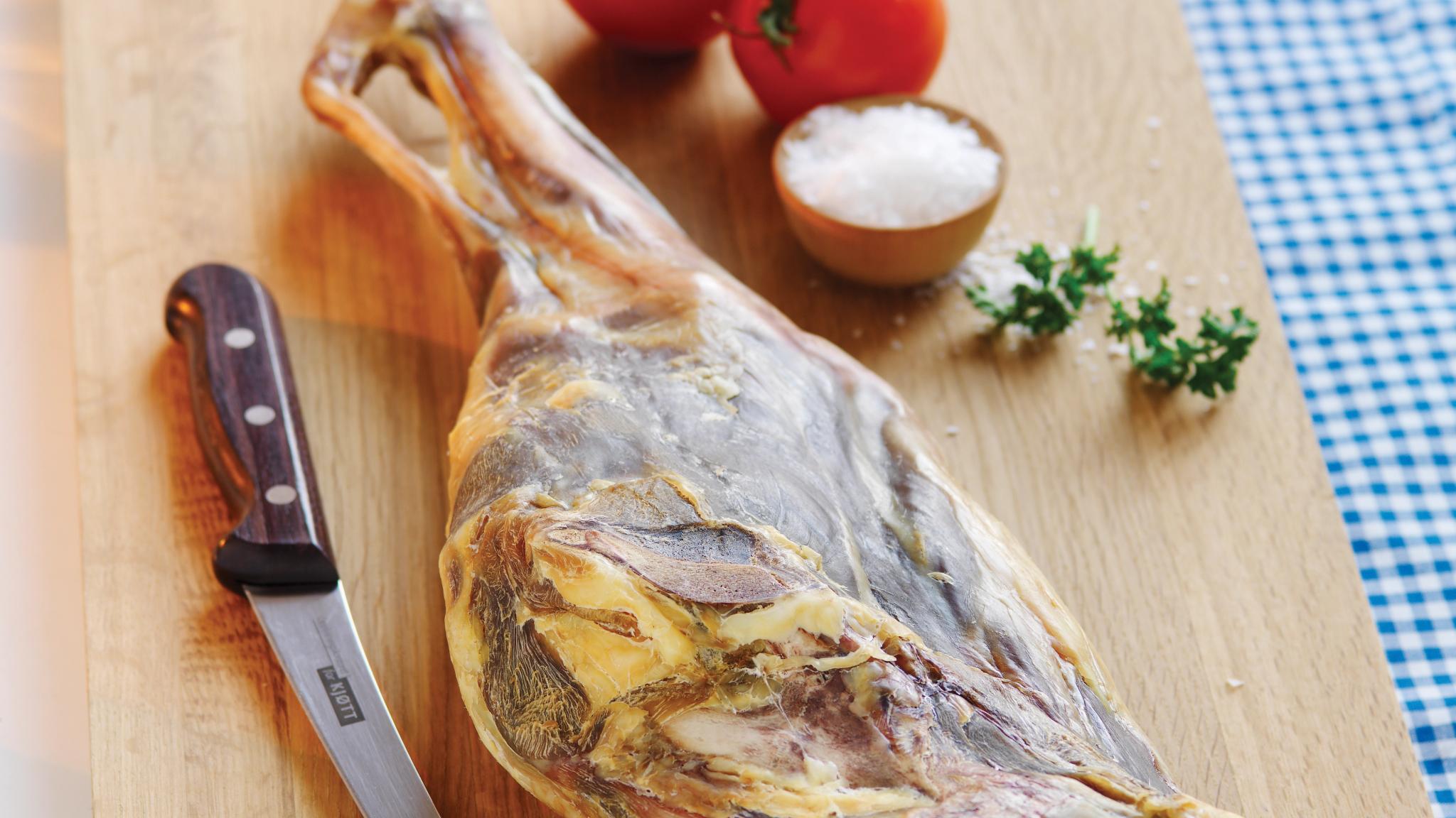 Fenalår on a cutting board with salt and tomatos