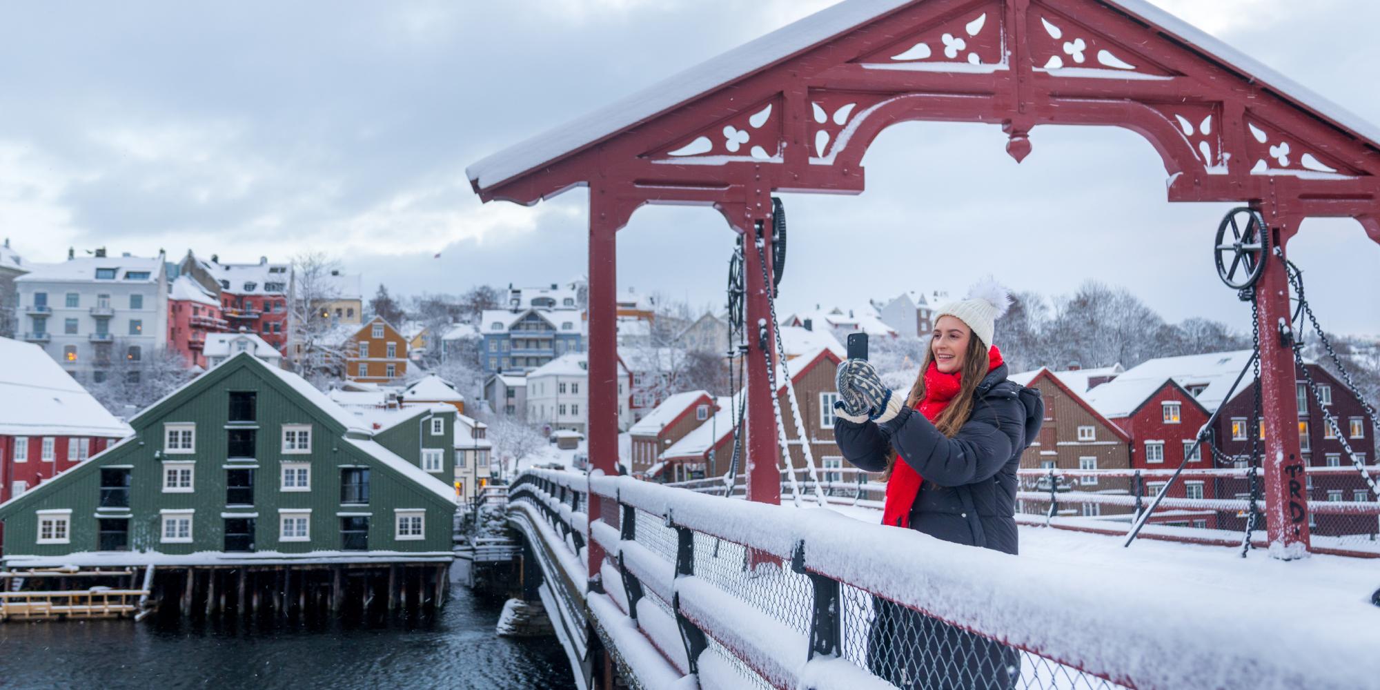 A women taking a picture from the Old Town Bridge in Trondheim in winter, Trøndelag, Norway.