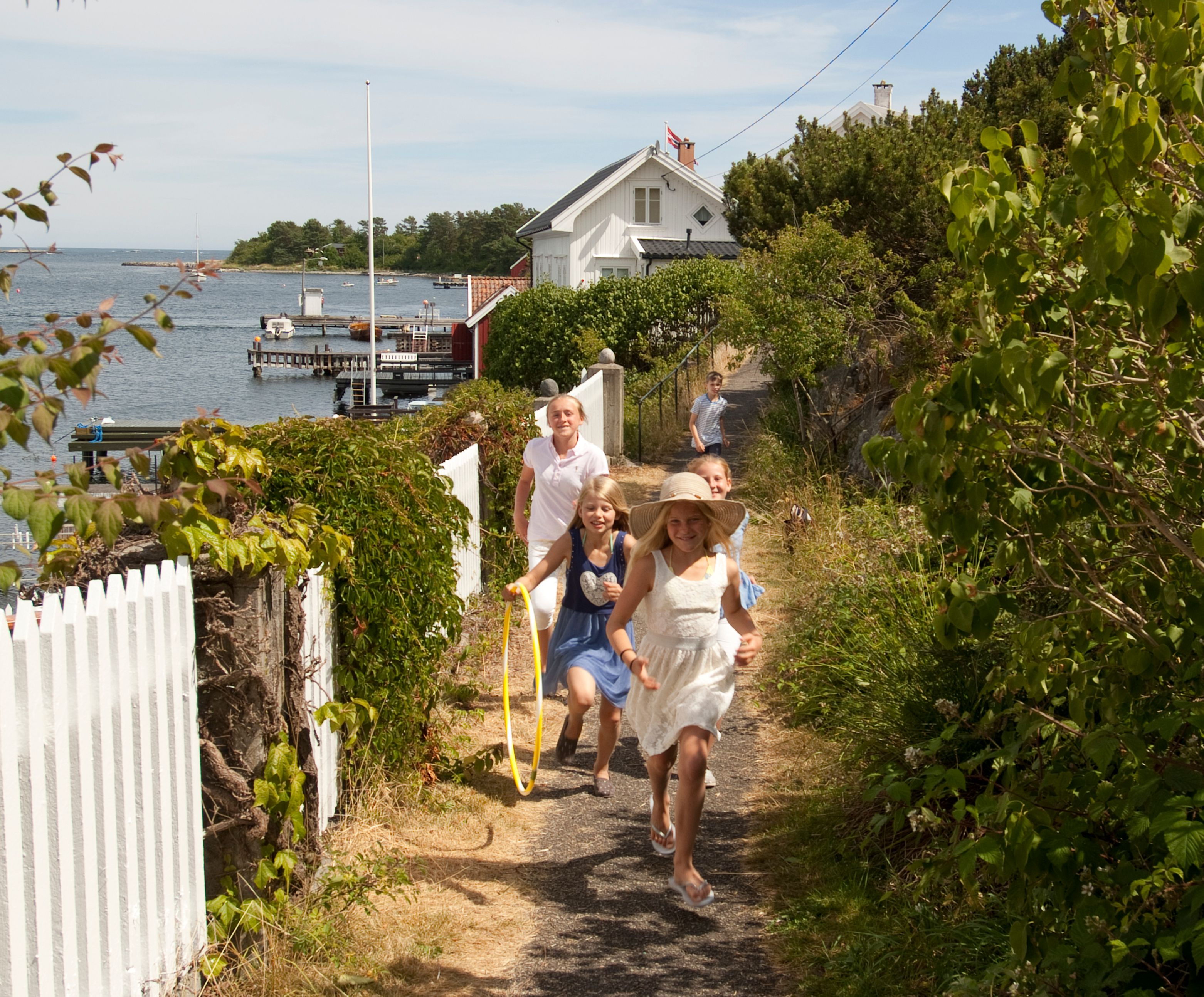 A group of children running along a white picket fence on Merdø island in Arendal, Southern Norway.