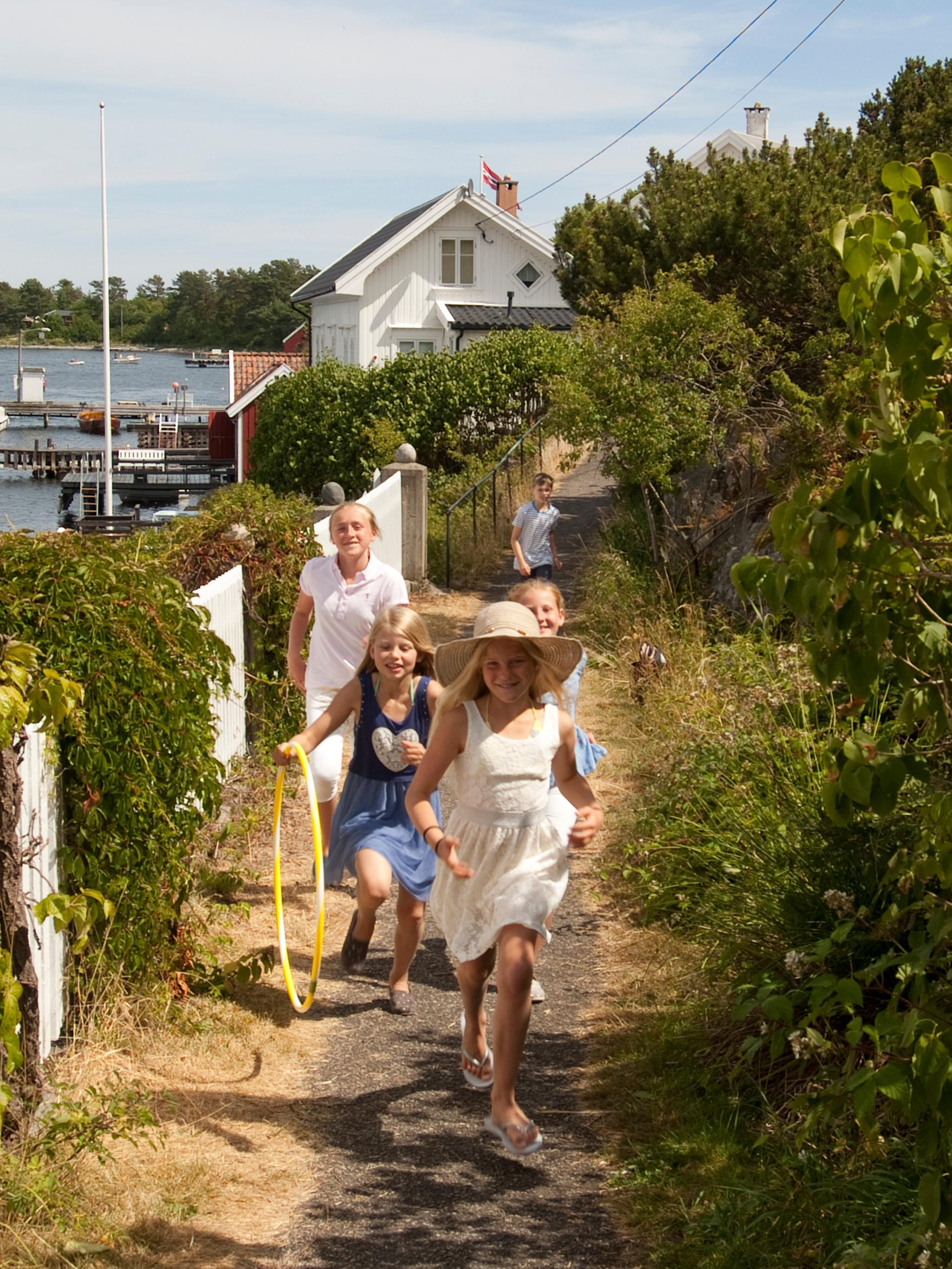 A group of children running along a white picket fence on Merdø island in Arendal, Southern Norway.